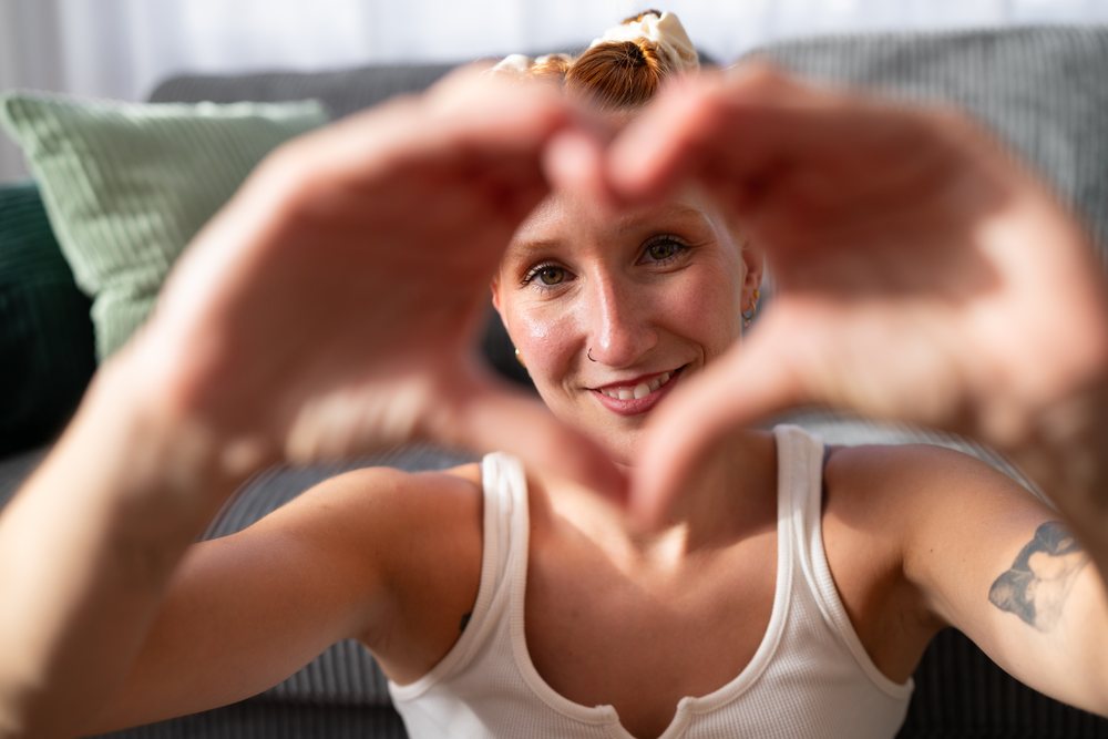 A young white woman forms a heart shape with her hands