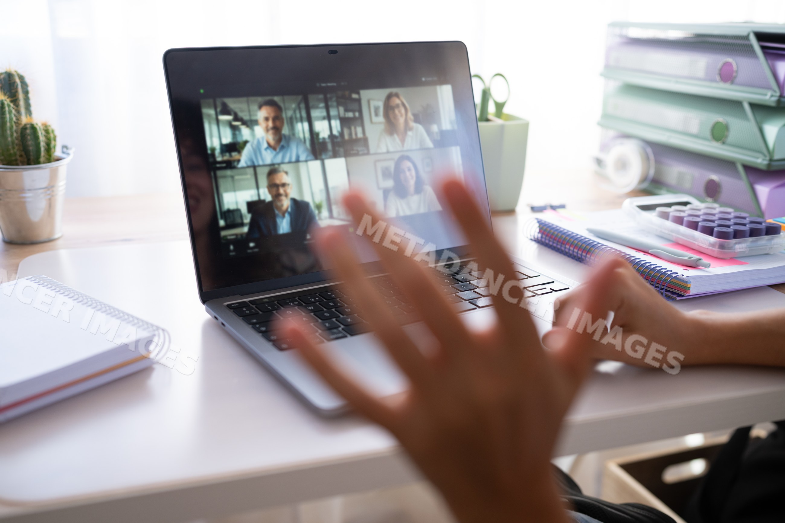 Hand waving during video call on laptop in home office setup