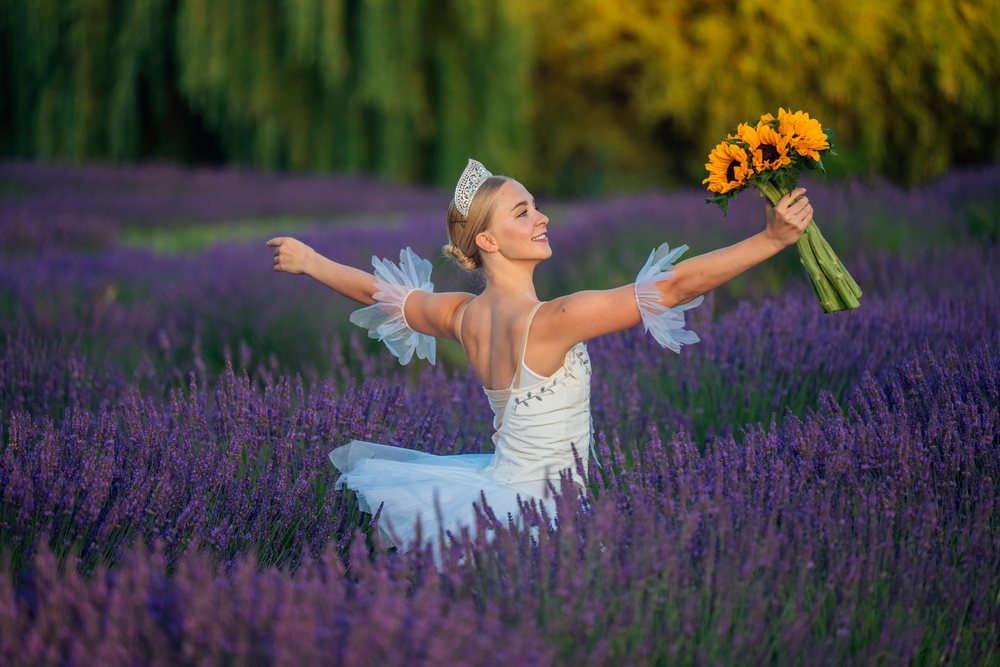 A ballet white dancer gracefully holds sunflowers in a lavender field