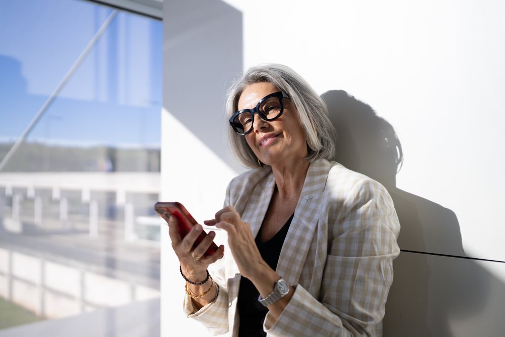 Middle-aged white woman using smartphone indoors near window in Madrid