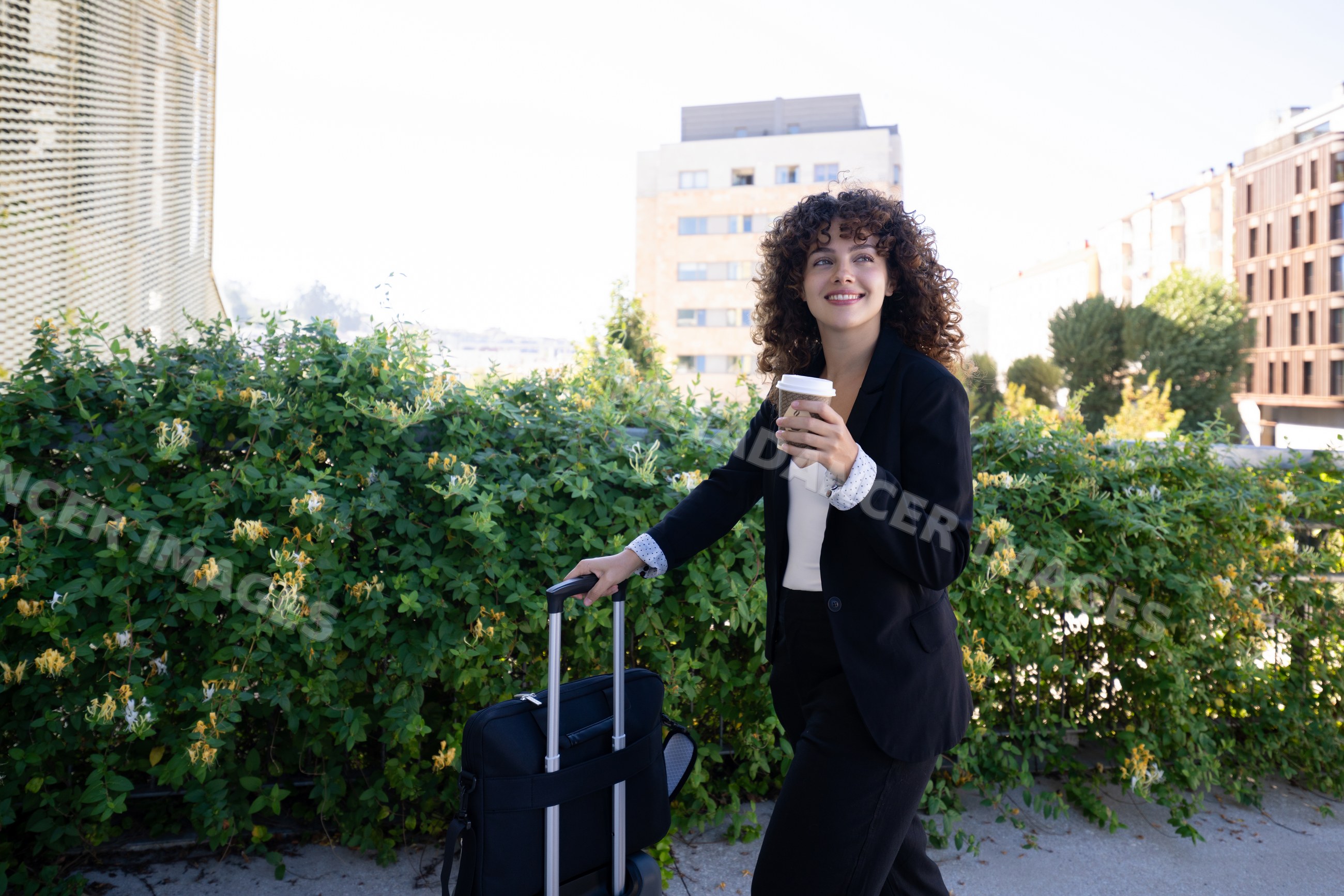 White woman walking with coffee cup and rolling suitcase