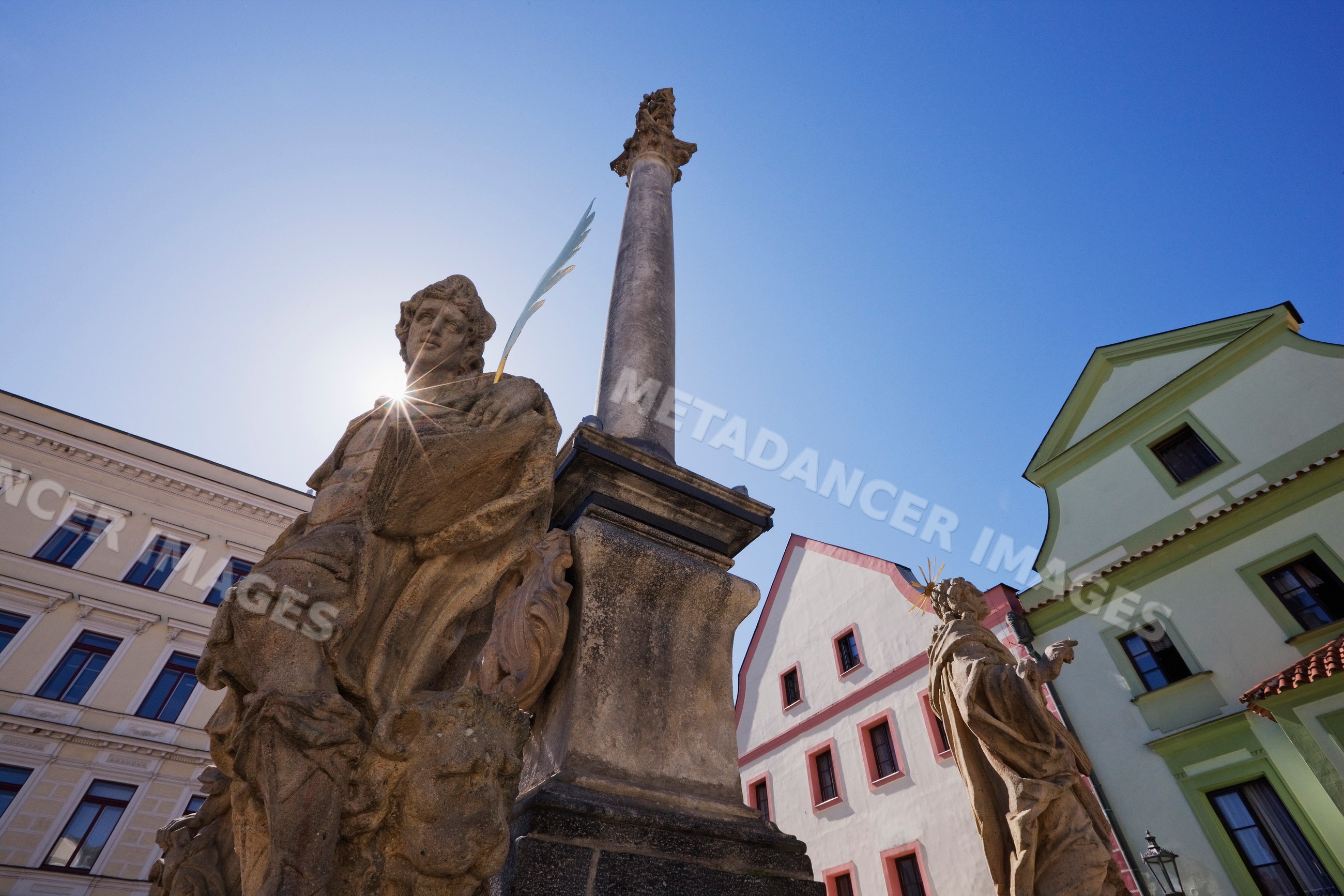 Statues and column in historic bohemian town square under blue sky