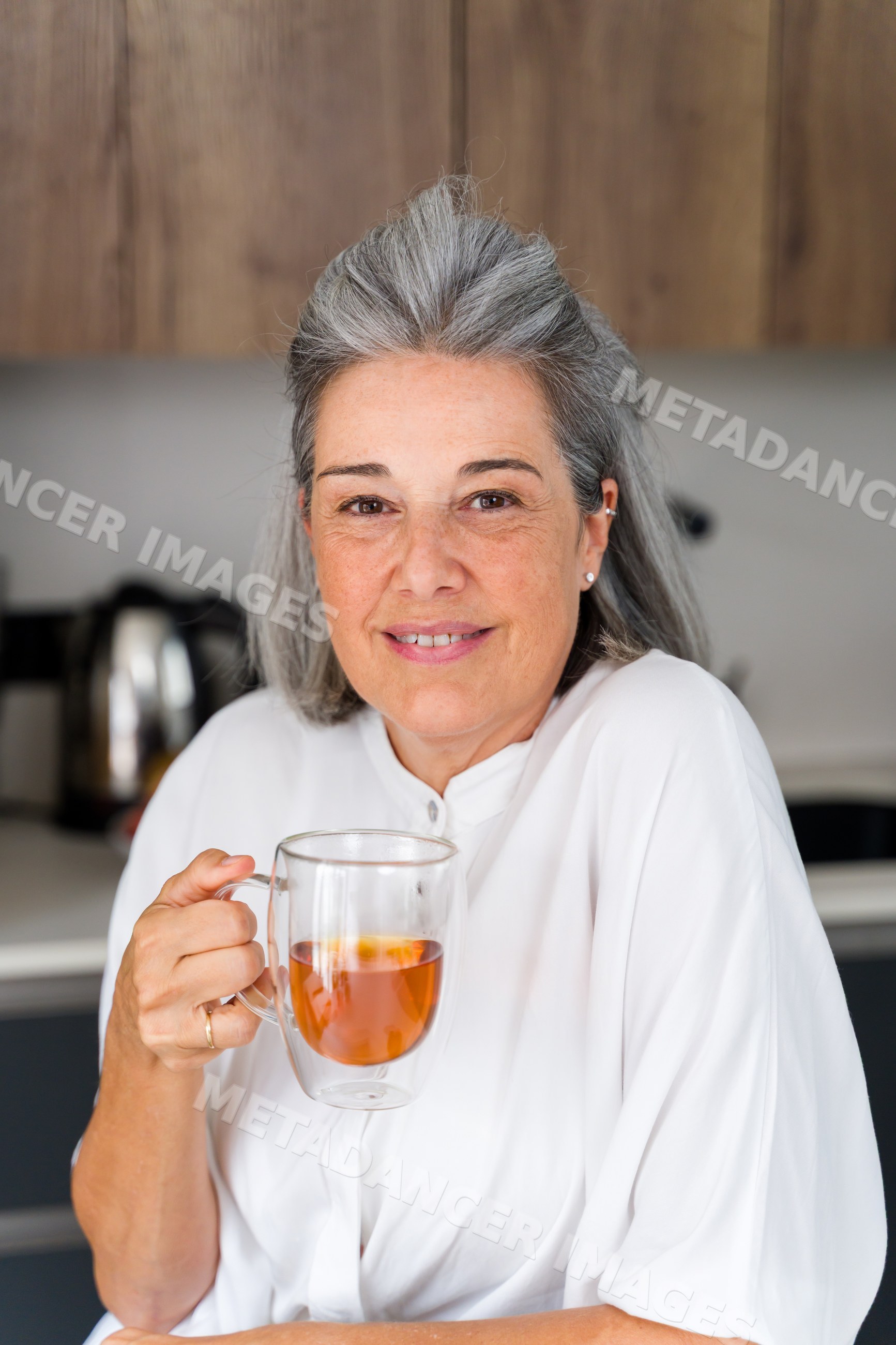 Mature white woman holding a glass mug of tea in kitchen