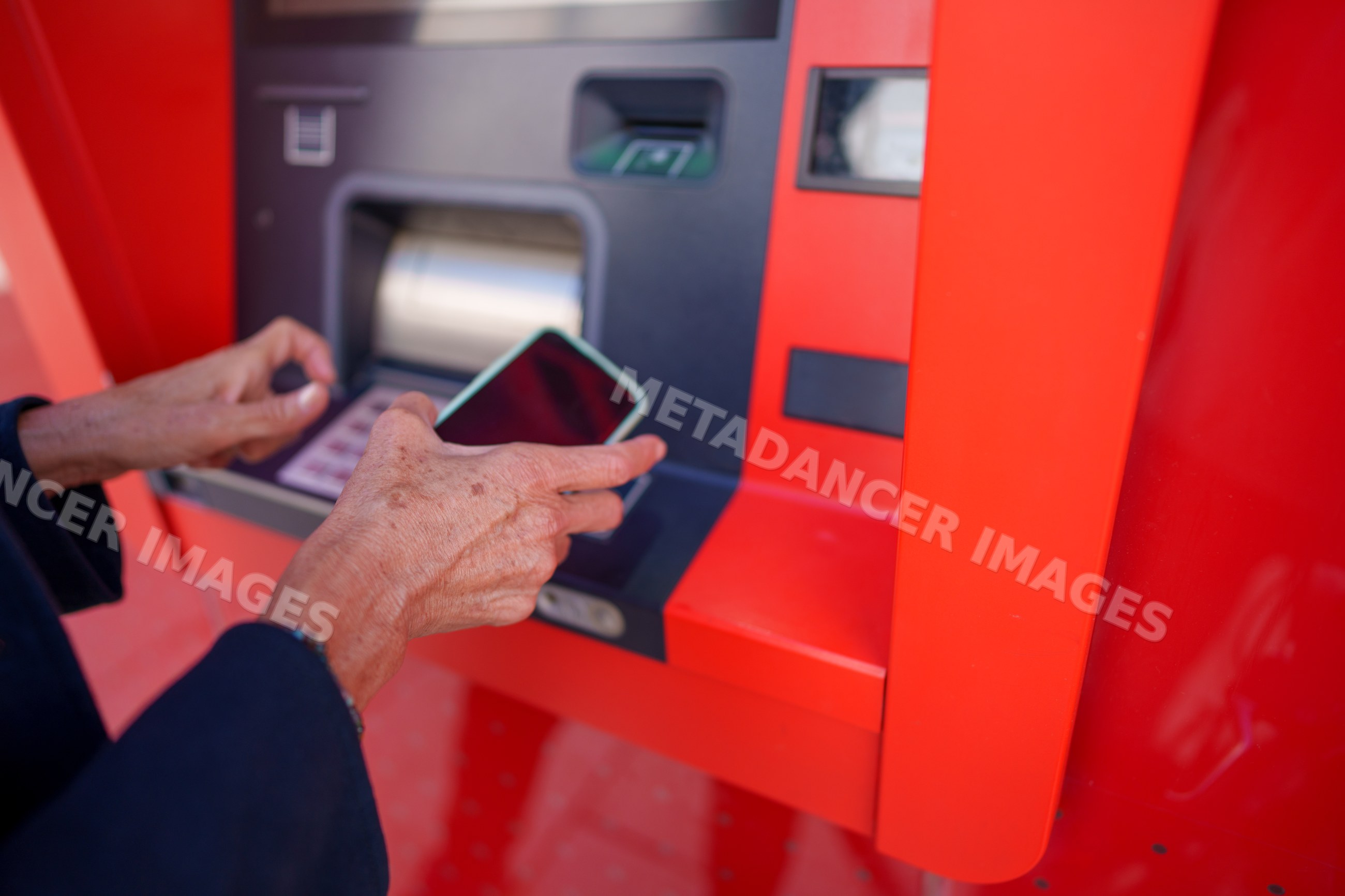 Hands using smartphone at red atm machine