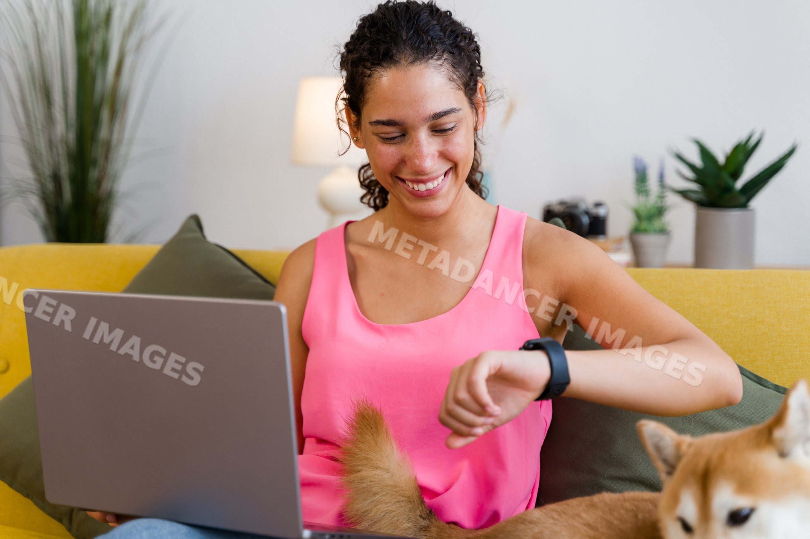A Hispanic woman smiling while checking her smartwatch on a yellow
