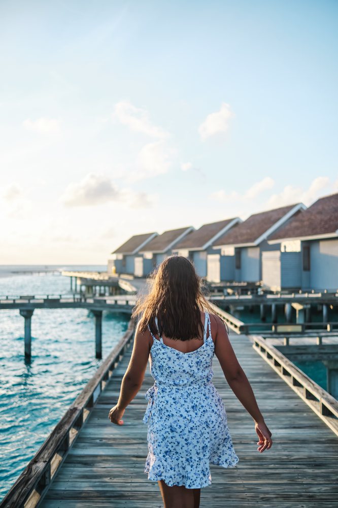 A white woman walks on a boardwalk toward overwater bungalows