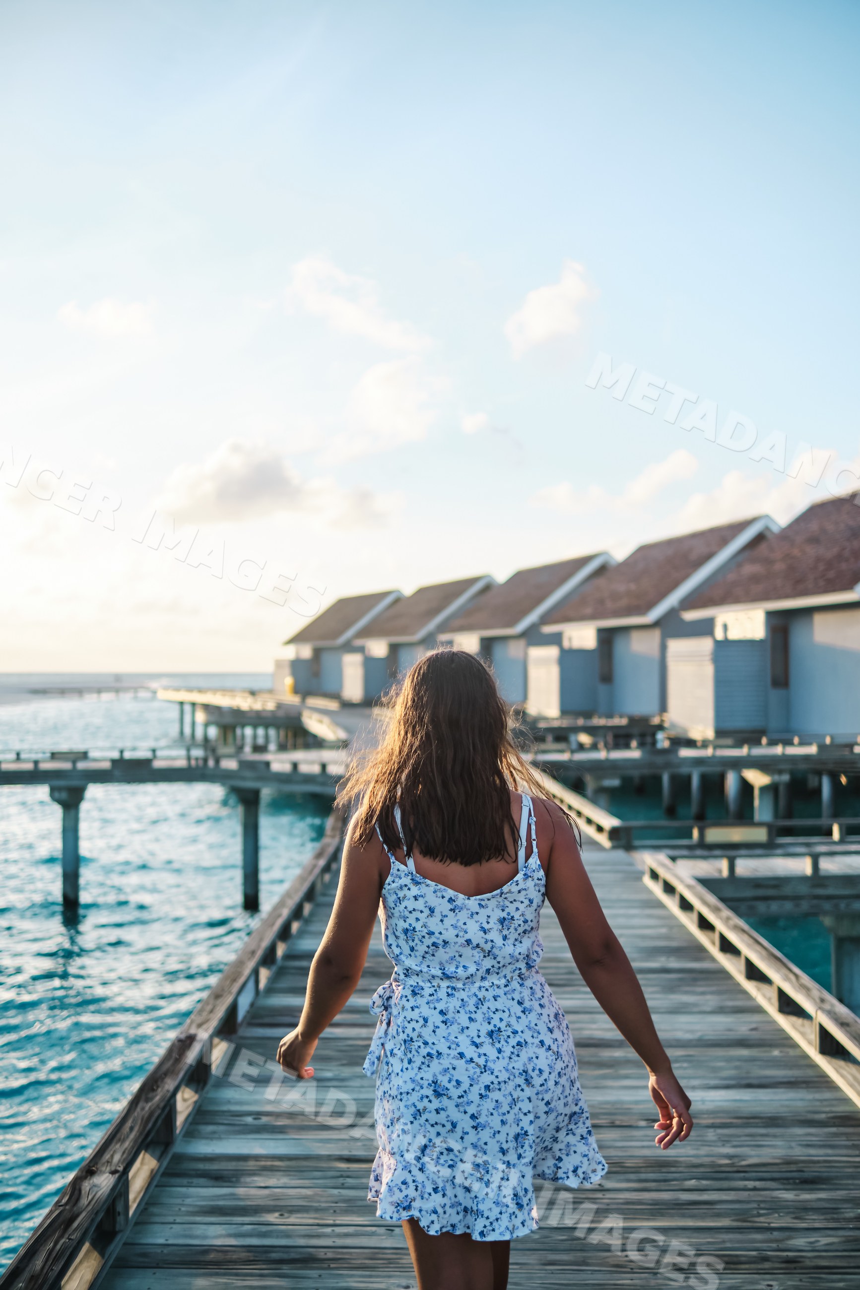 A white woman walks on a boardwalk toward overwater bungalows