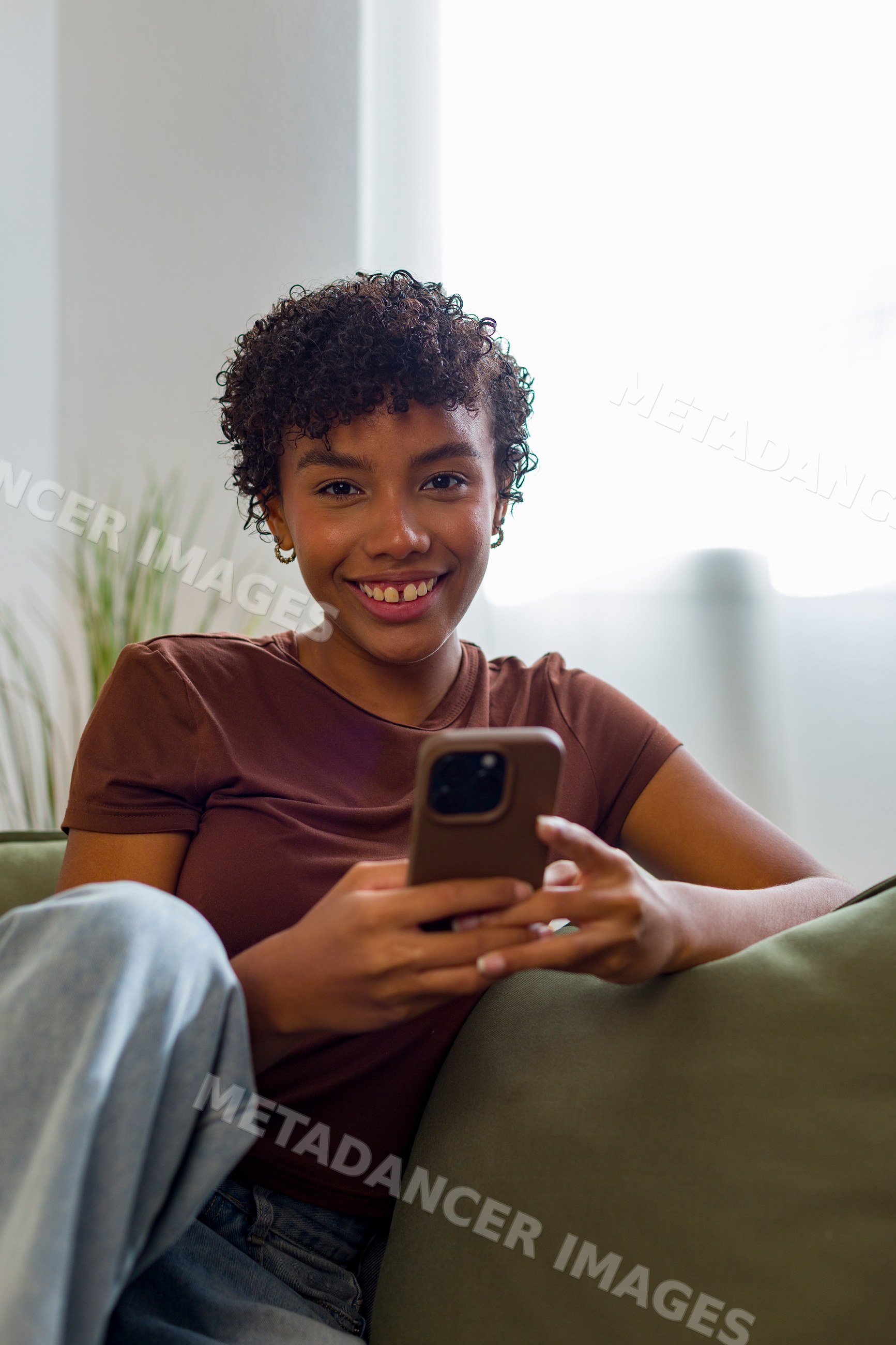 Young African American woman happily using smartphone sitting on couch
