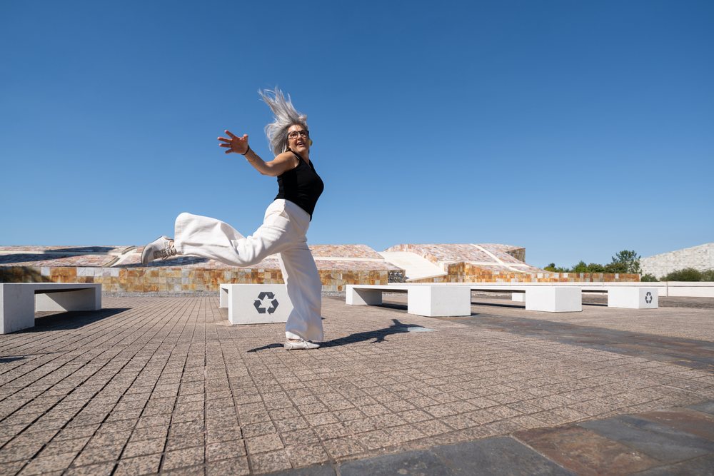 White woman jumping joyfully in a sunlit public square
