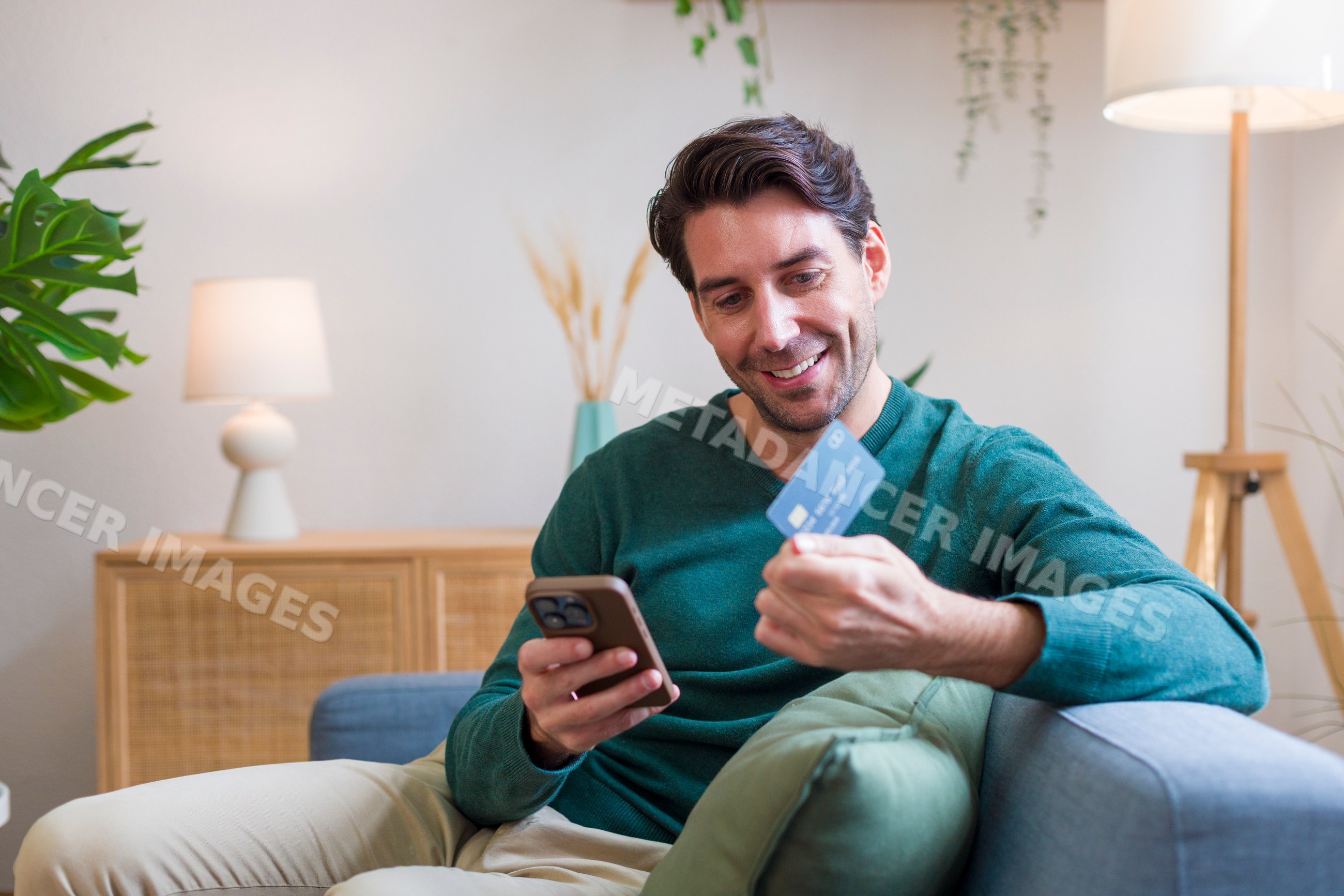 White man using smartphone and credit card sitting on sofa
