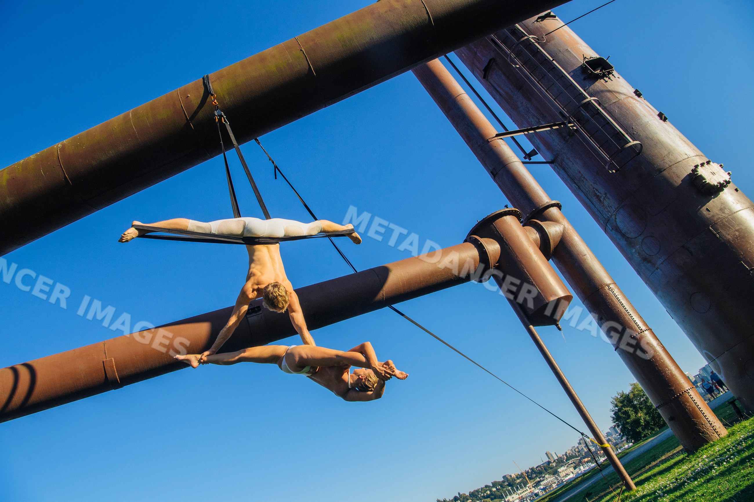 Two aerialists perform acrobatics suspended from outdoor metal