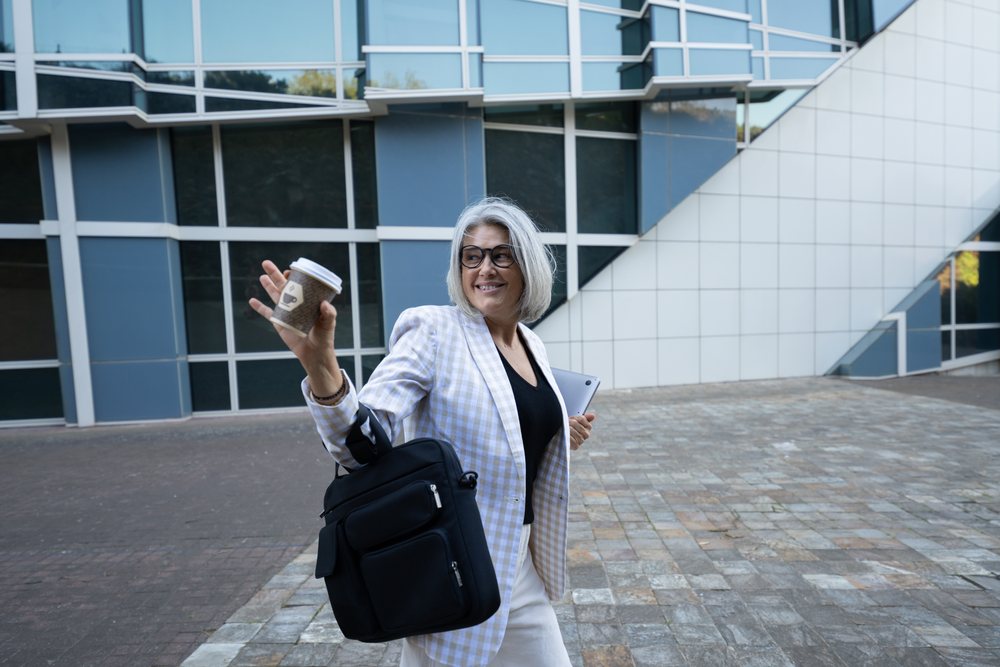 Businesswoman carrying coffee cup and tablet walking outside office