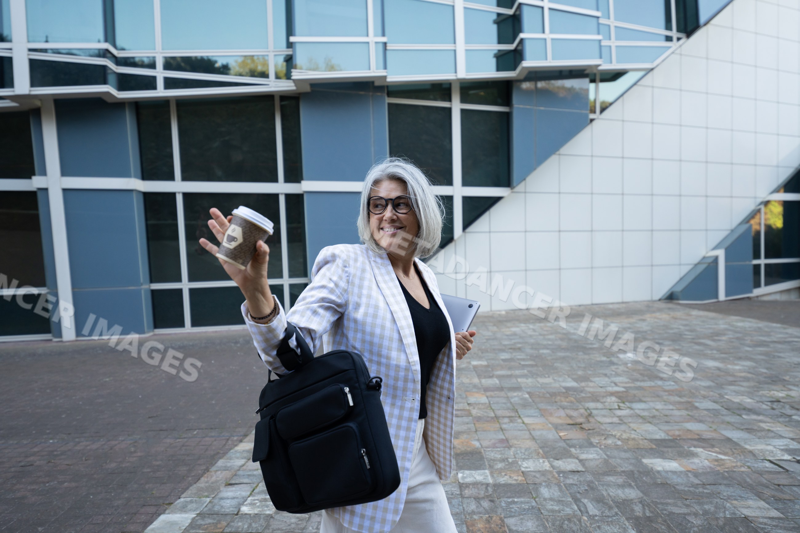 Businesswoman carrying coffee cup and tablet walking outside office