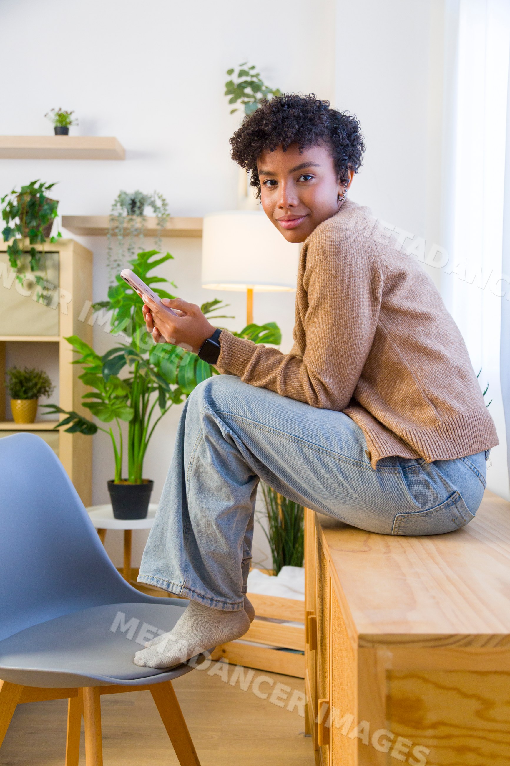 Young African American woman using smartphone seated on wooden cabinet
