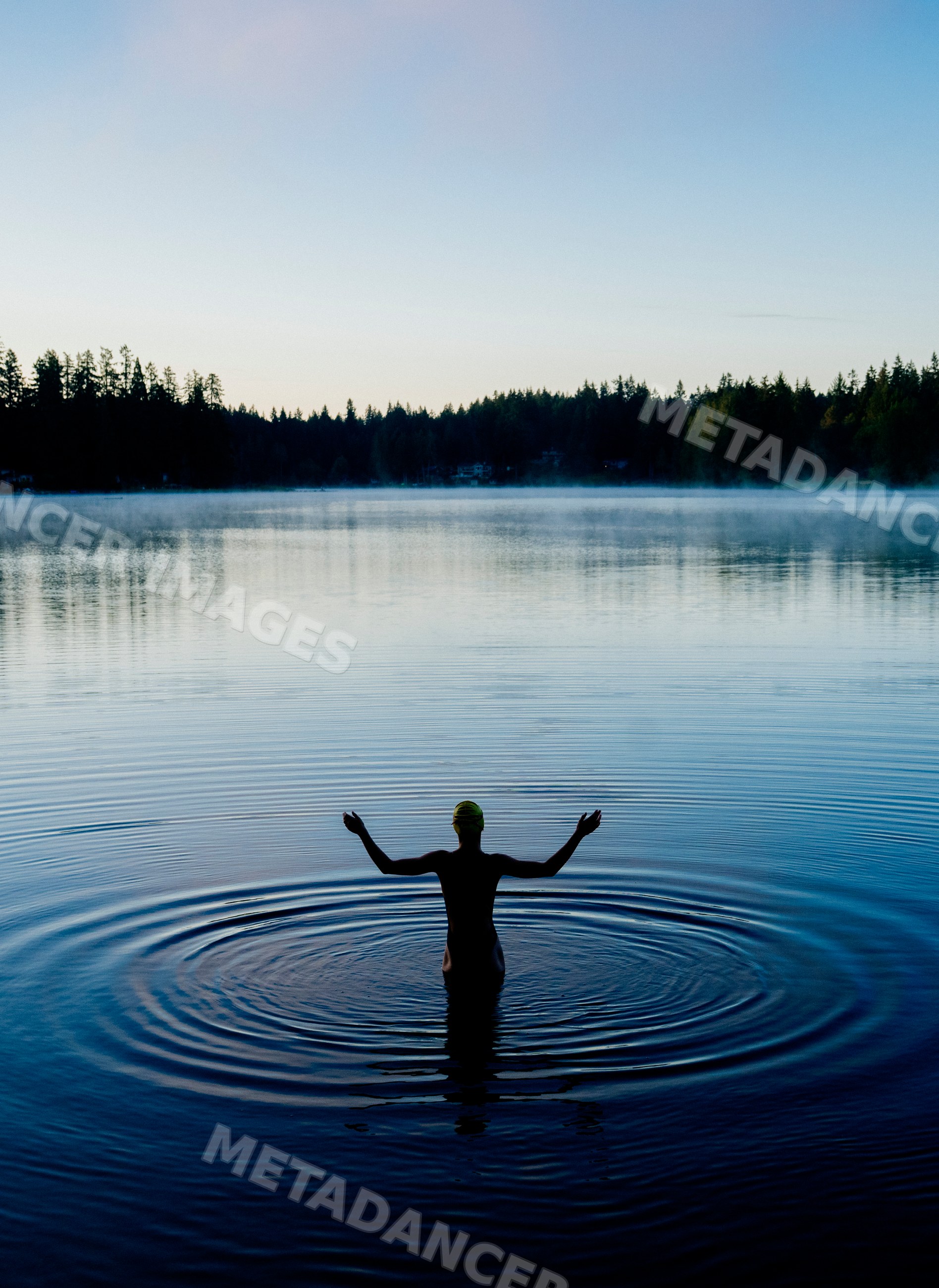 White person standing in calm lake water with forest and morning mist