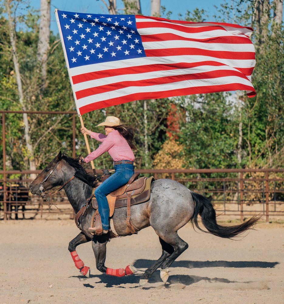 White woman riding horse holding american flag in western arena