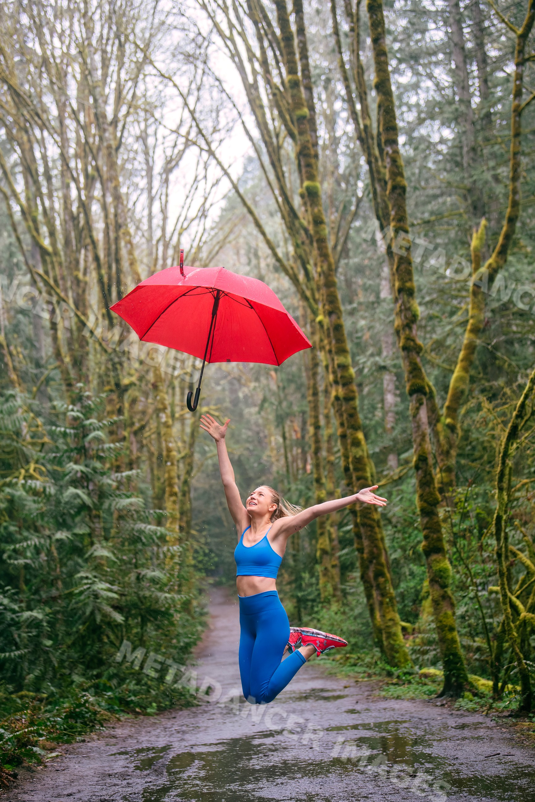 White woman jumping with red umbrella on wet forest trail