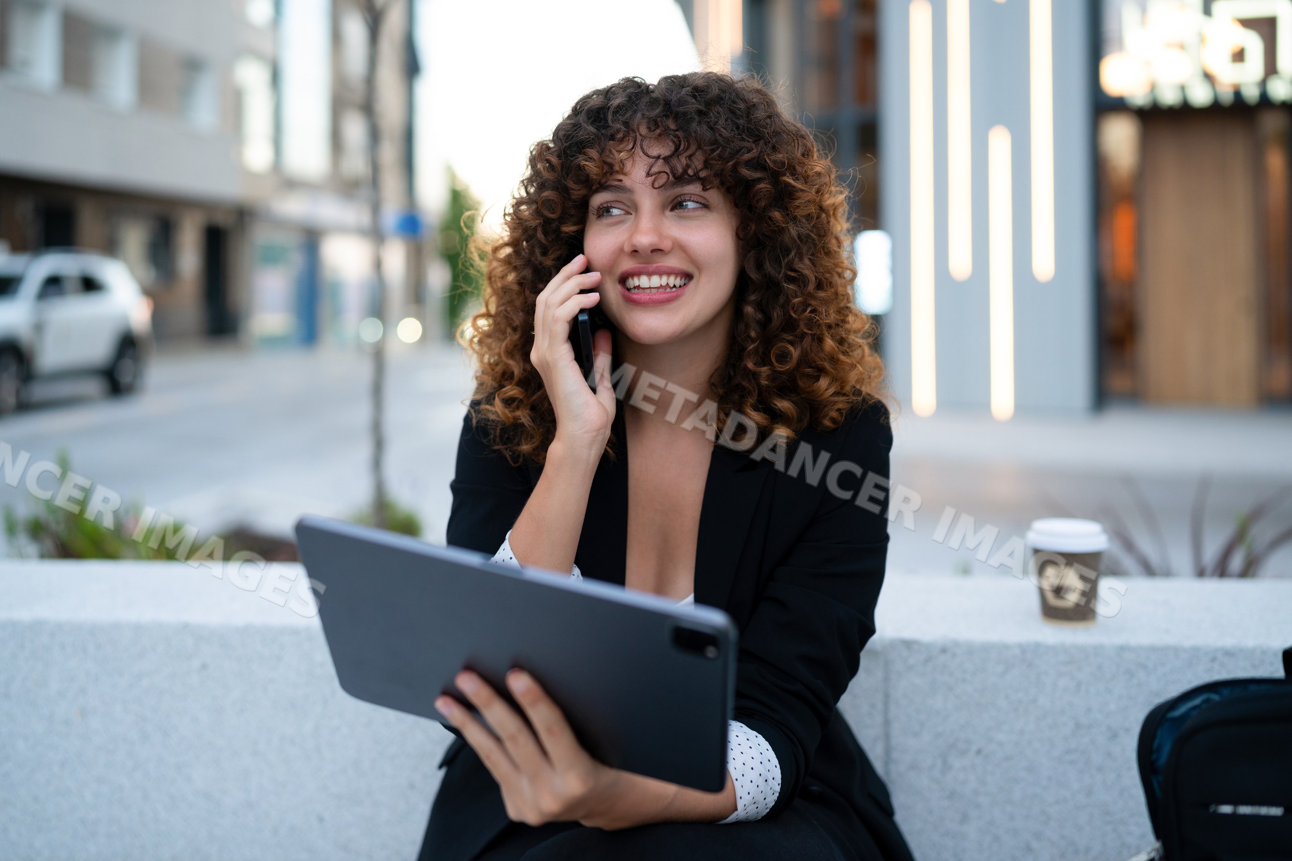 Young white woman holding tablet and talking on phone outdoors