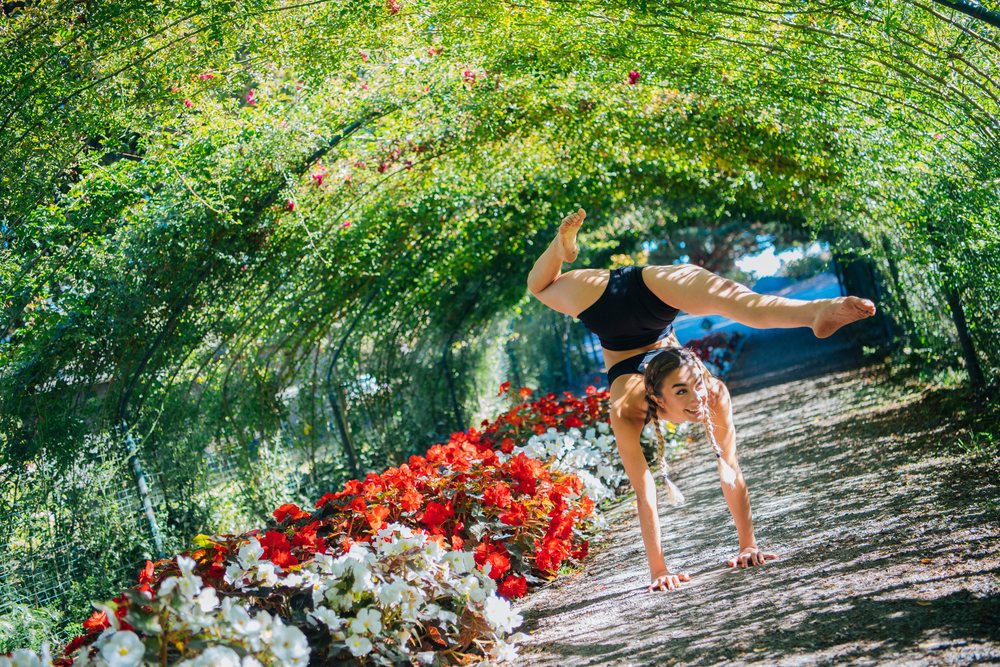 White woman doing a handstand on garden path with flowers