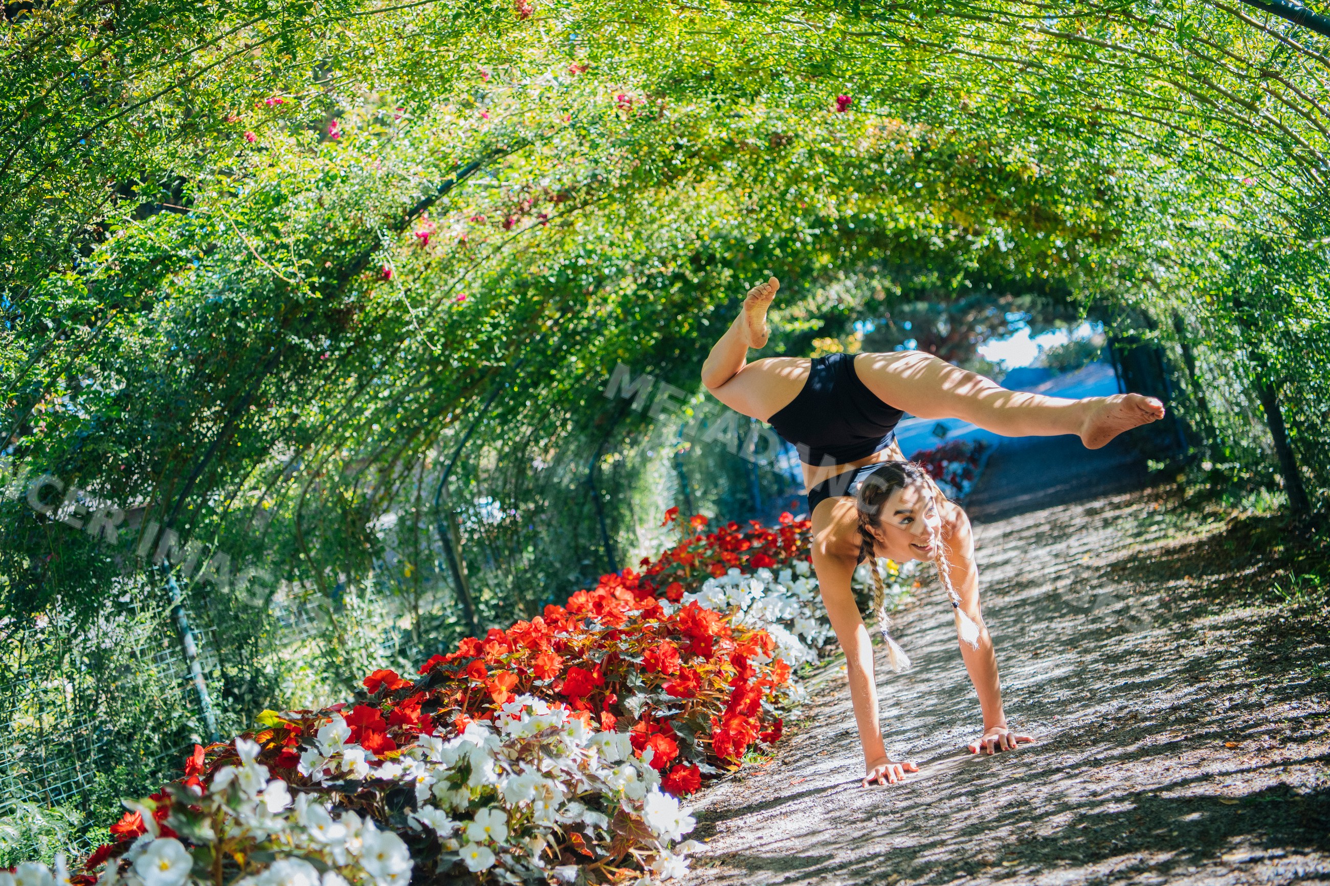 White woman doing a handstand on garden path with flowers