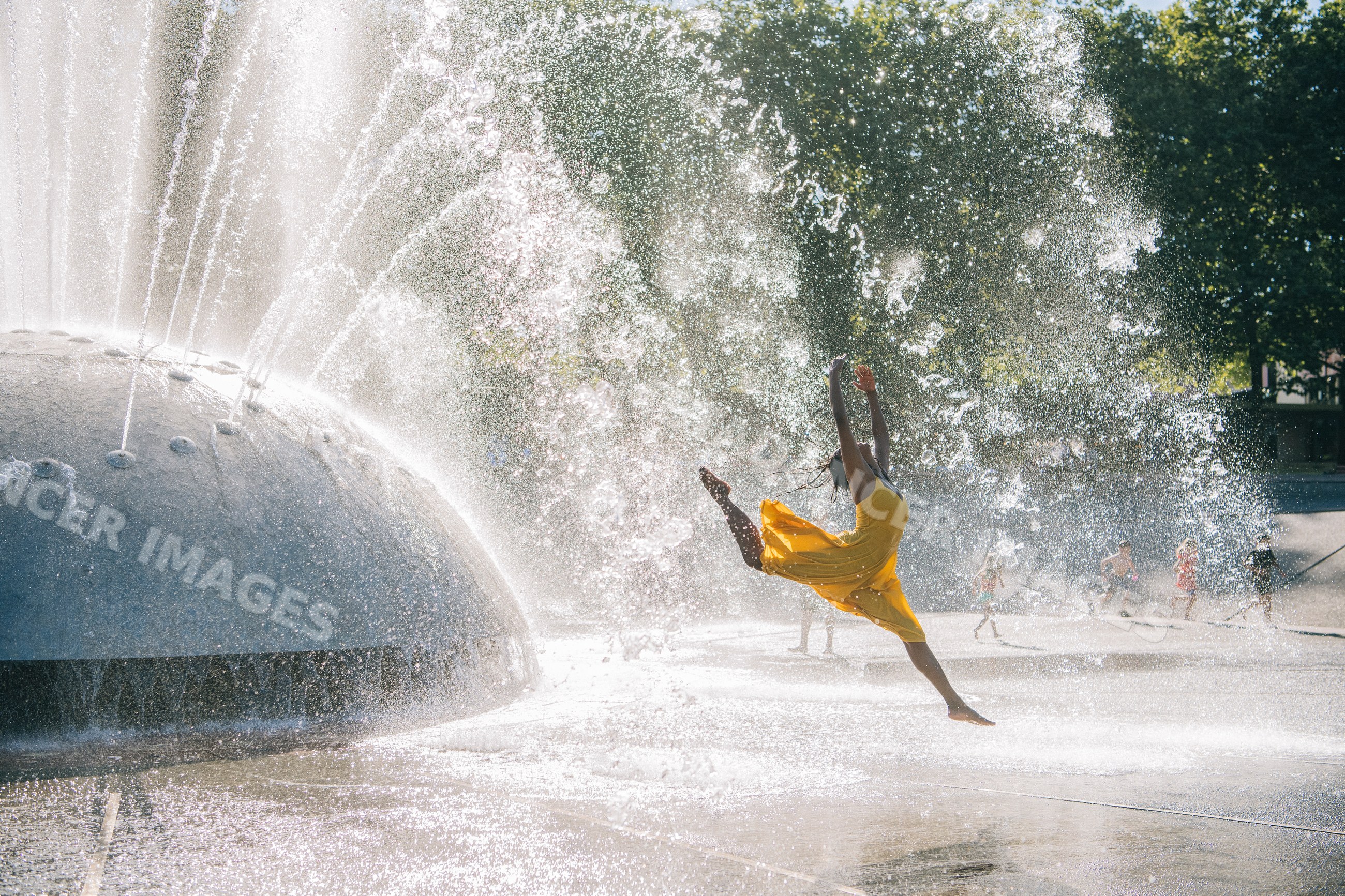 South Asian woman jumping through water fountain spray on sunny day