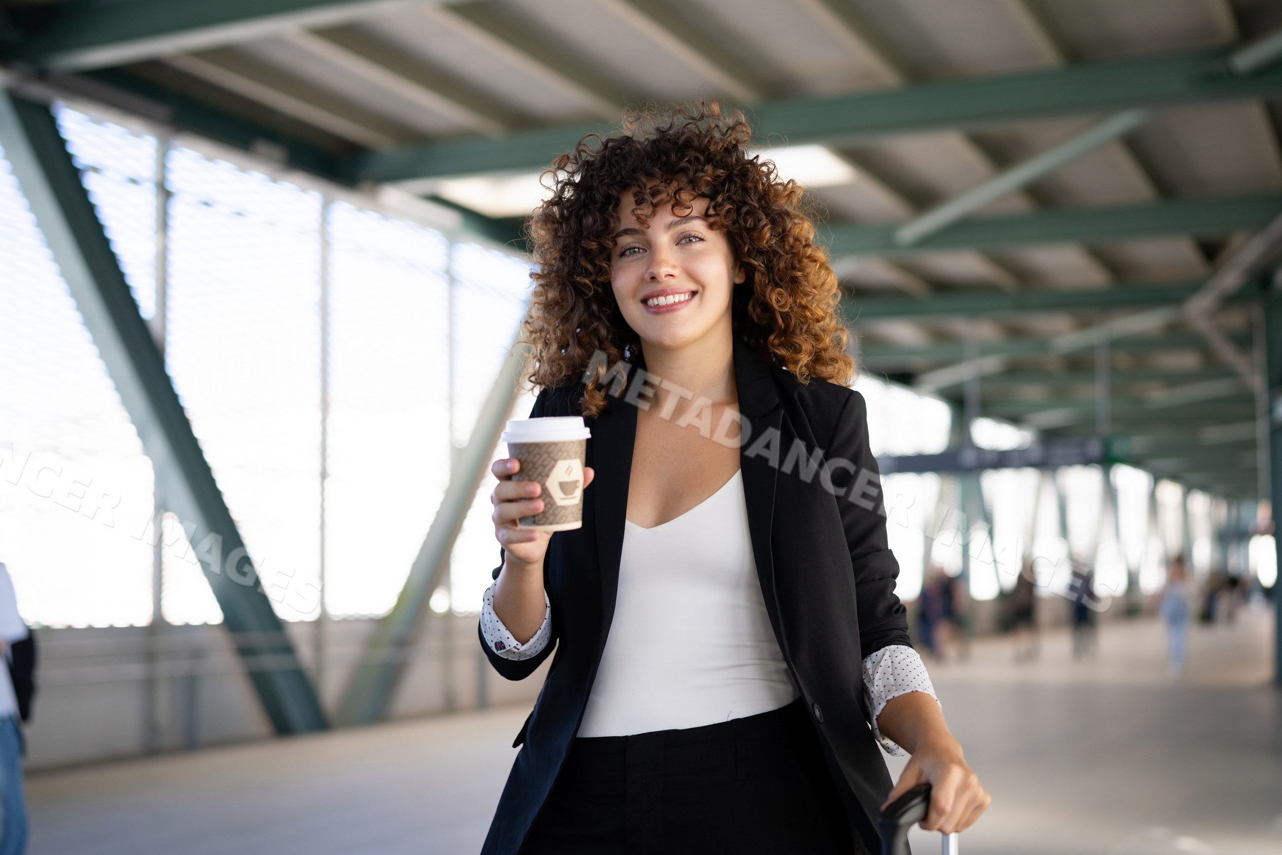 White woman with coffee walking through airport terminal corridor