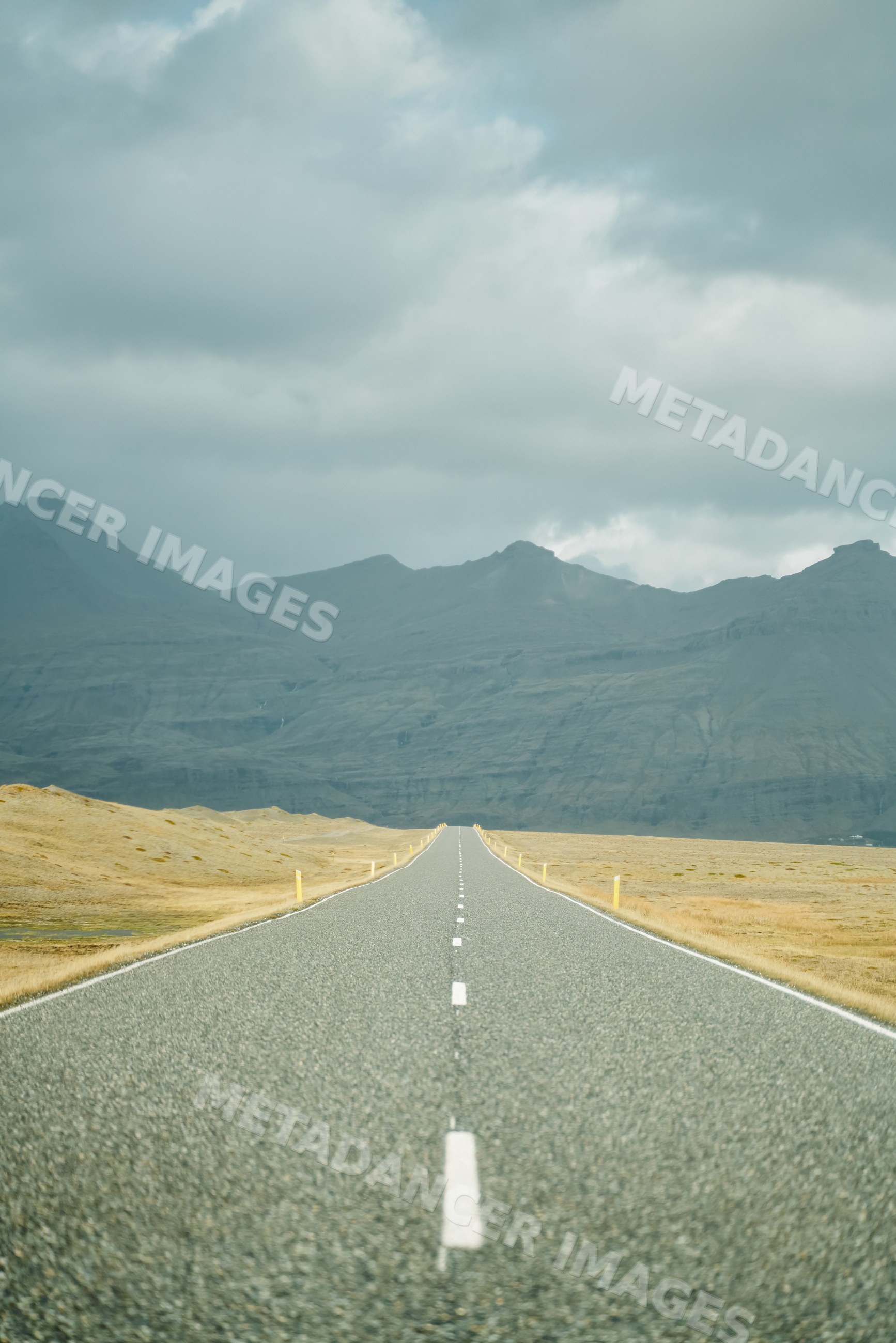 A straight road leads through grassy fields toward mountains