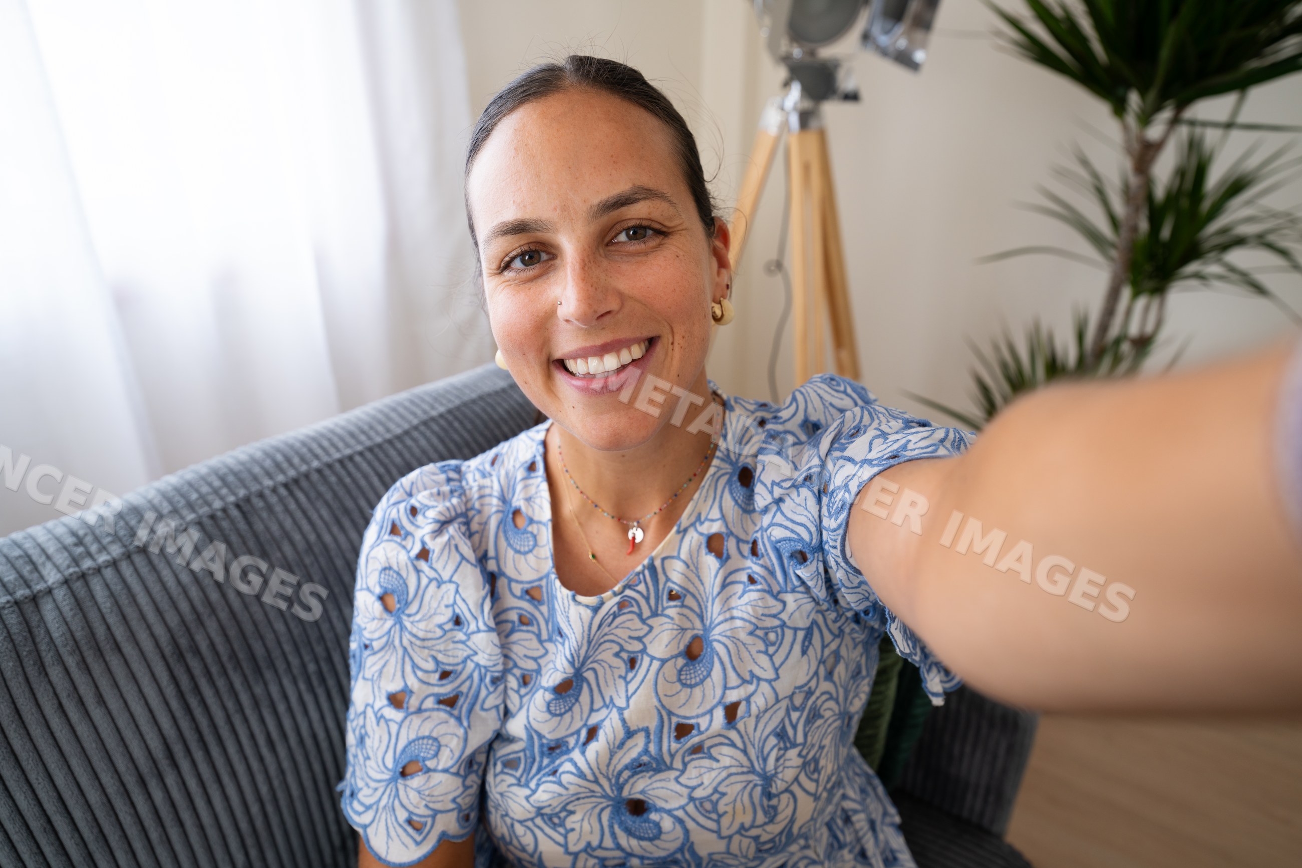 White woman smiling taking selfie indoors on couch with plant and lamp