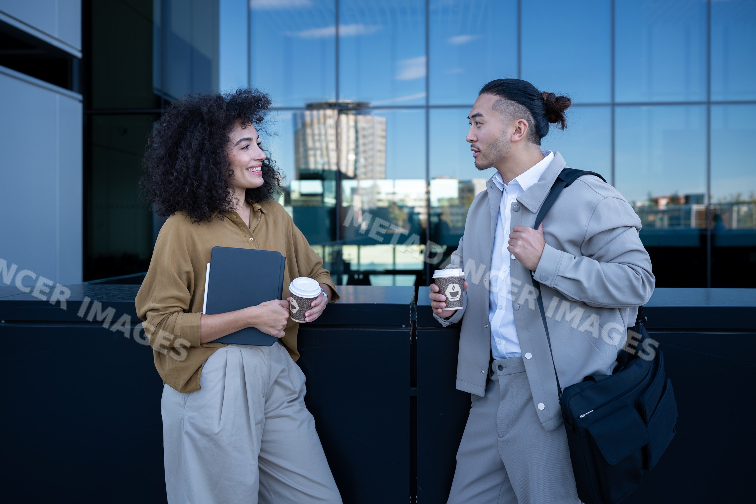 Two people chatting with coffee cups outside modern office building