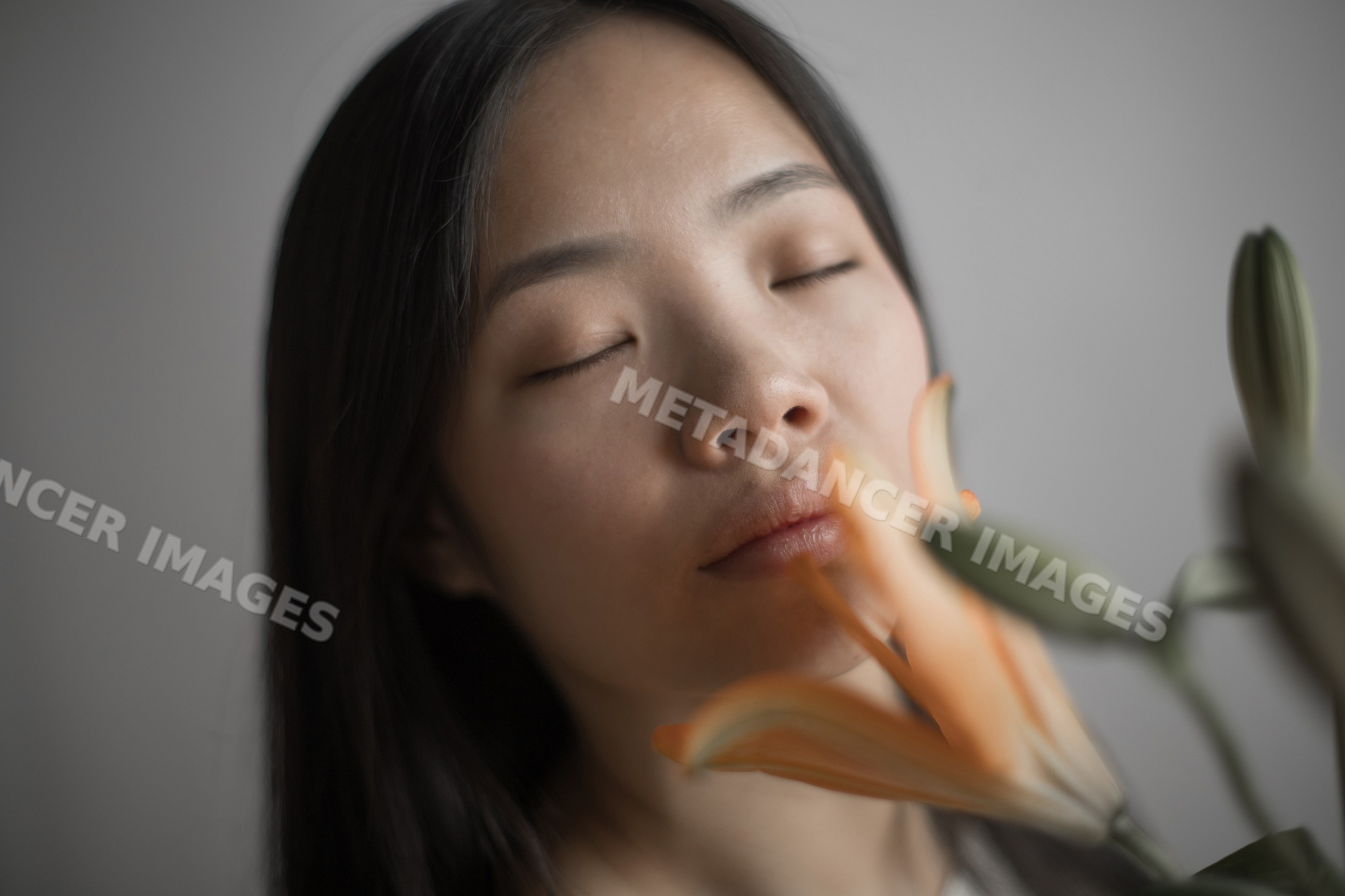 Southeast Asian woman enjoying orange lily flower with closed eyes