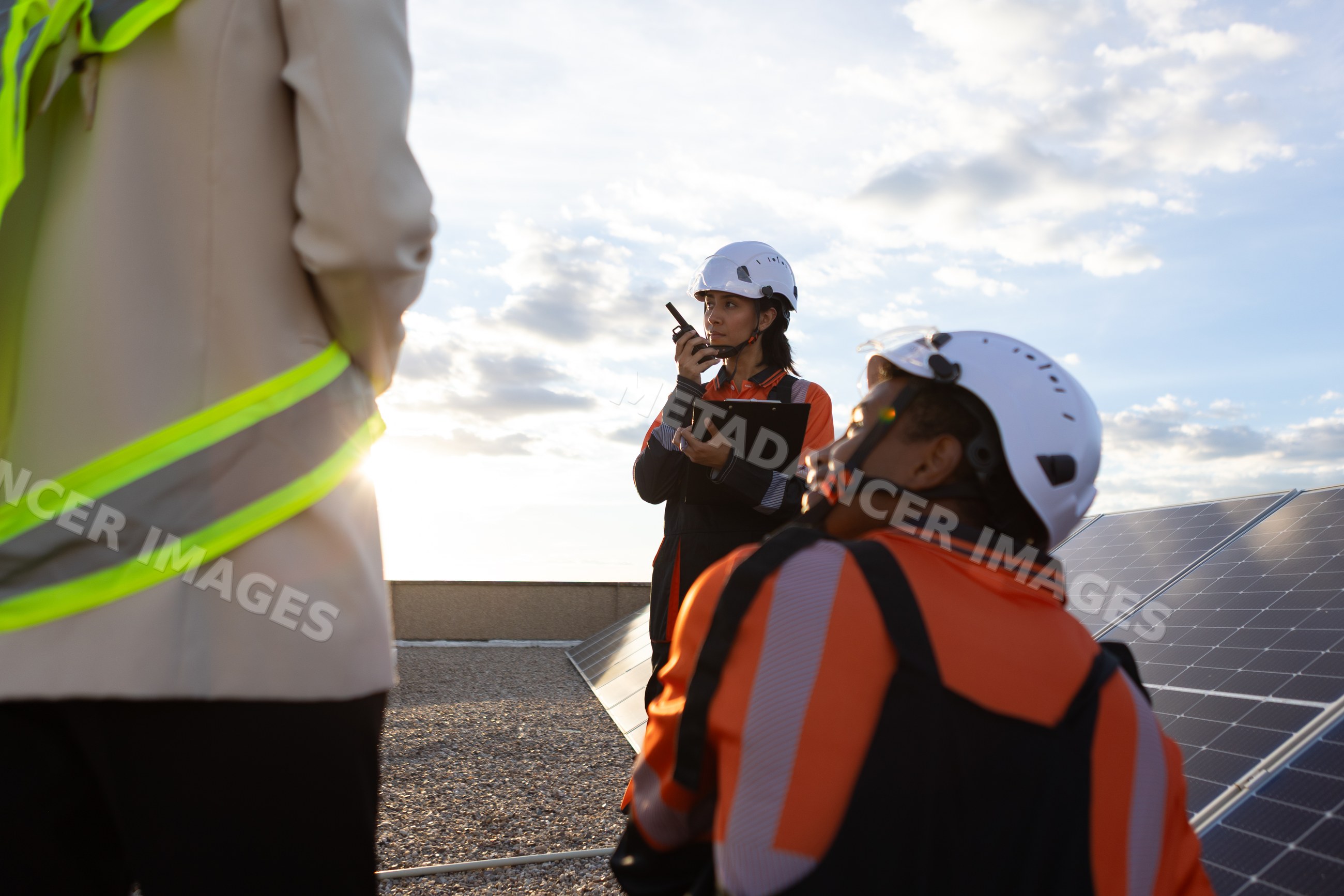 Hispanic and white workers communicating near solar panels at sunset