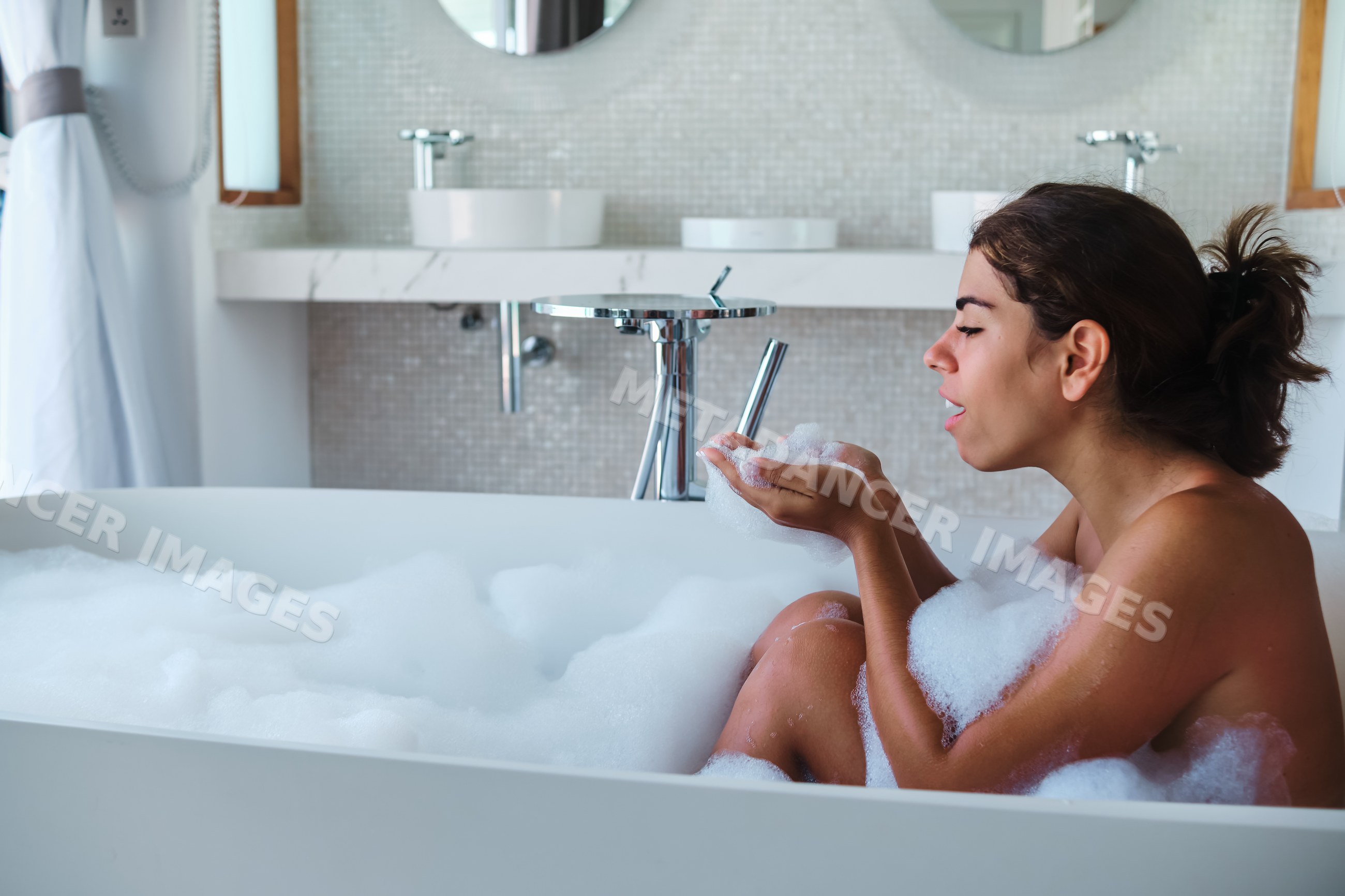 A white woman enjoys a relaxing bubble bath in a modern bathroom