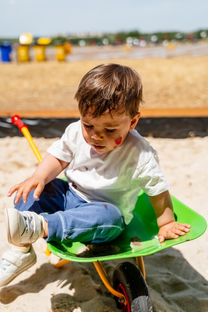 White child playing in wheelbarrow at sandbox playground in Spain