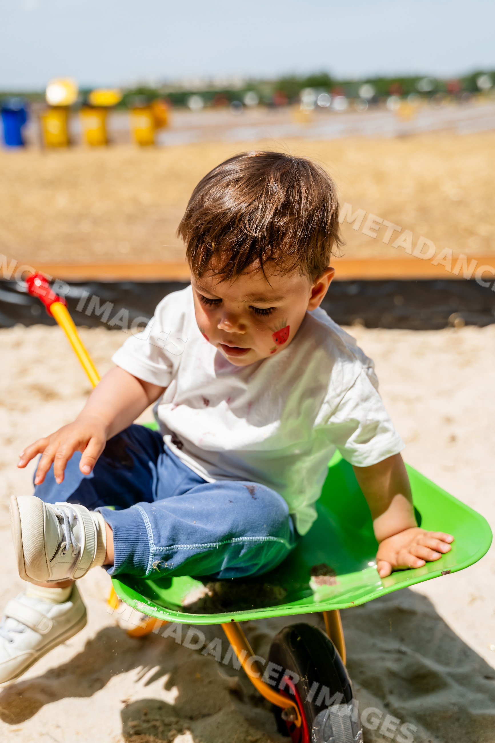 White child playing in wheelbarrow at sandbox playground in Spain