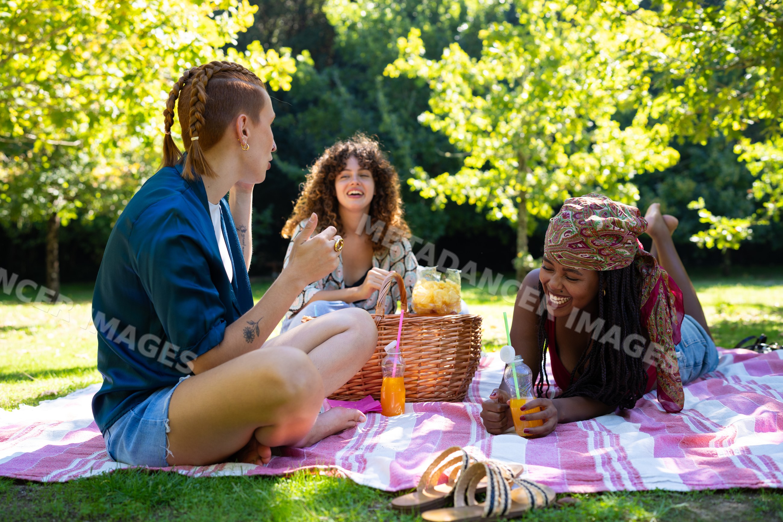 Friends enjoying a sunny outdoor picnic on grass with juice and snacks