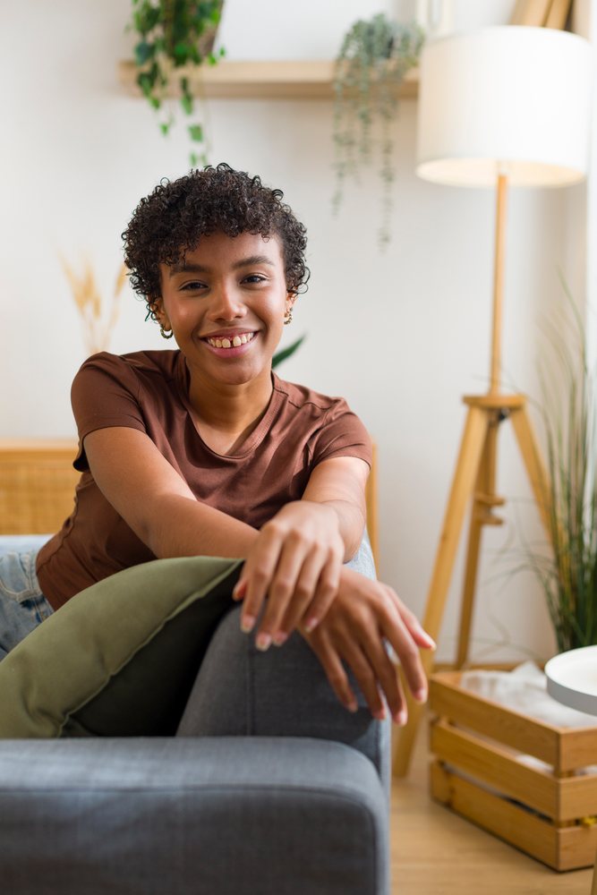 Young African American woman smiling on gray sofa in cozy living room