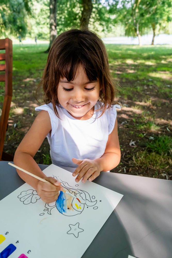 White child painting fish drawing with watercolors outdoors