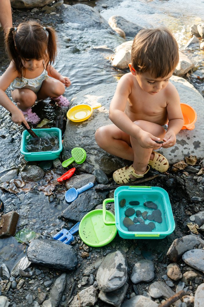 Two white children playing with water and rocks outdoors by a stream