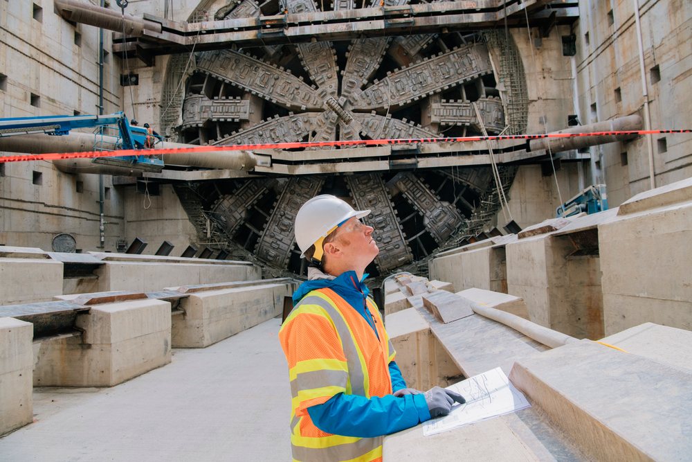 White construction worker inspects blueprints by a tunnel boring