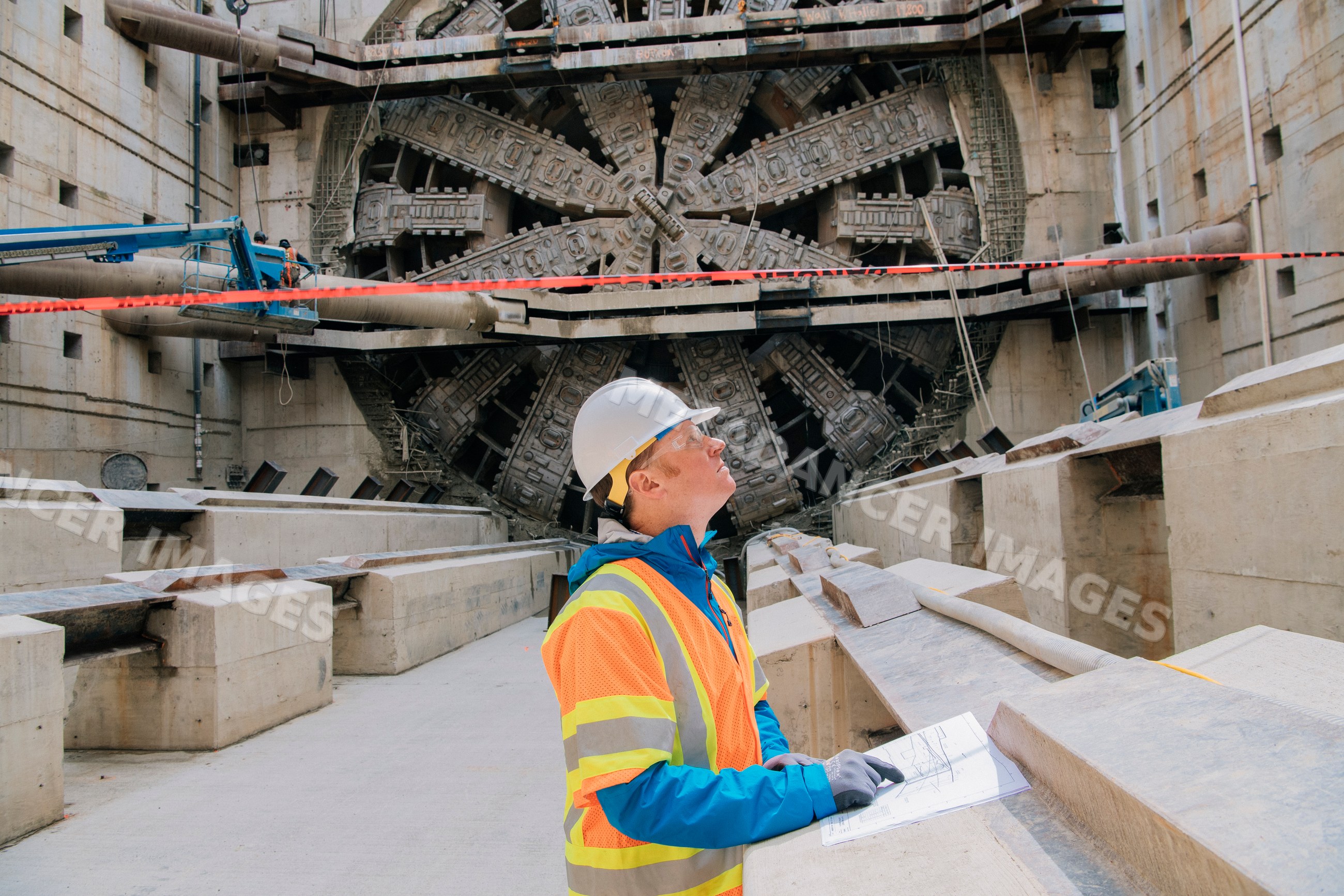 A construction white worker inspects blueprints by a tunnel boring
