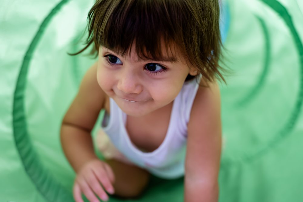 Baby crawling and smiling inside a green play tunnel