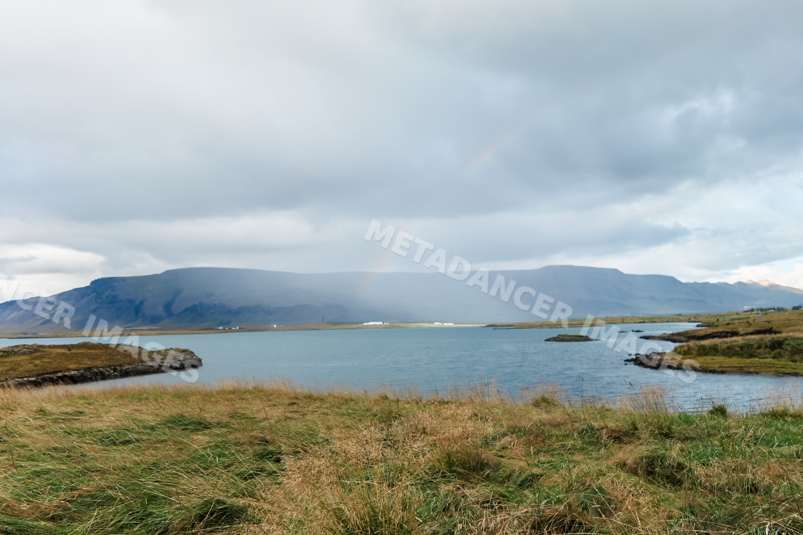 A rainbow appears over a lakeside mountain landscape