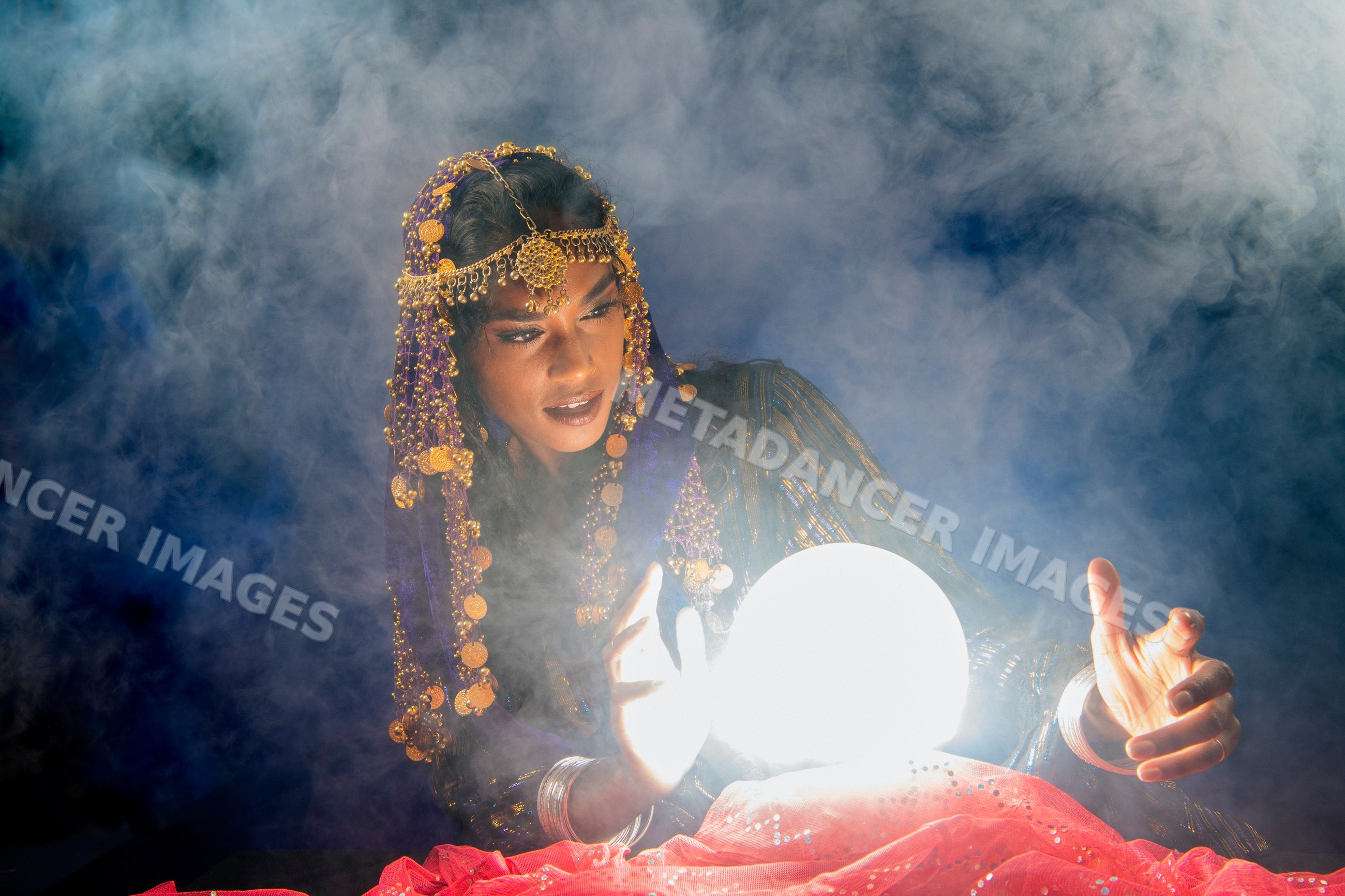 A South Asian woman dressed as a fortune teller gazes into a glowing