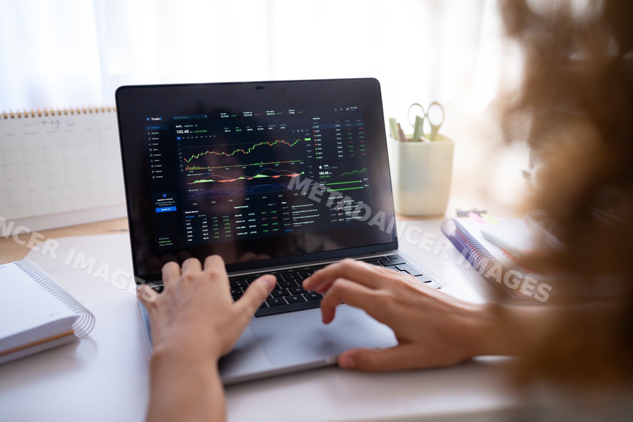 Hands typing on laptop showing stock market charts and financial data