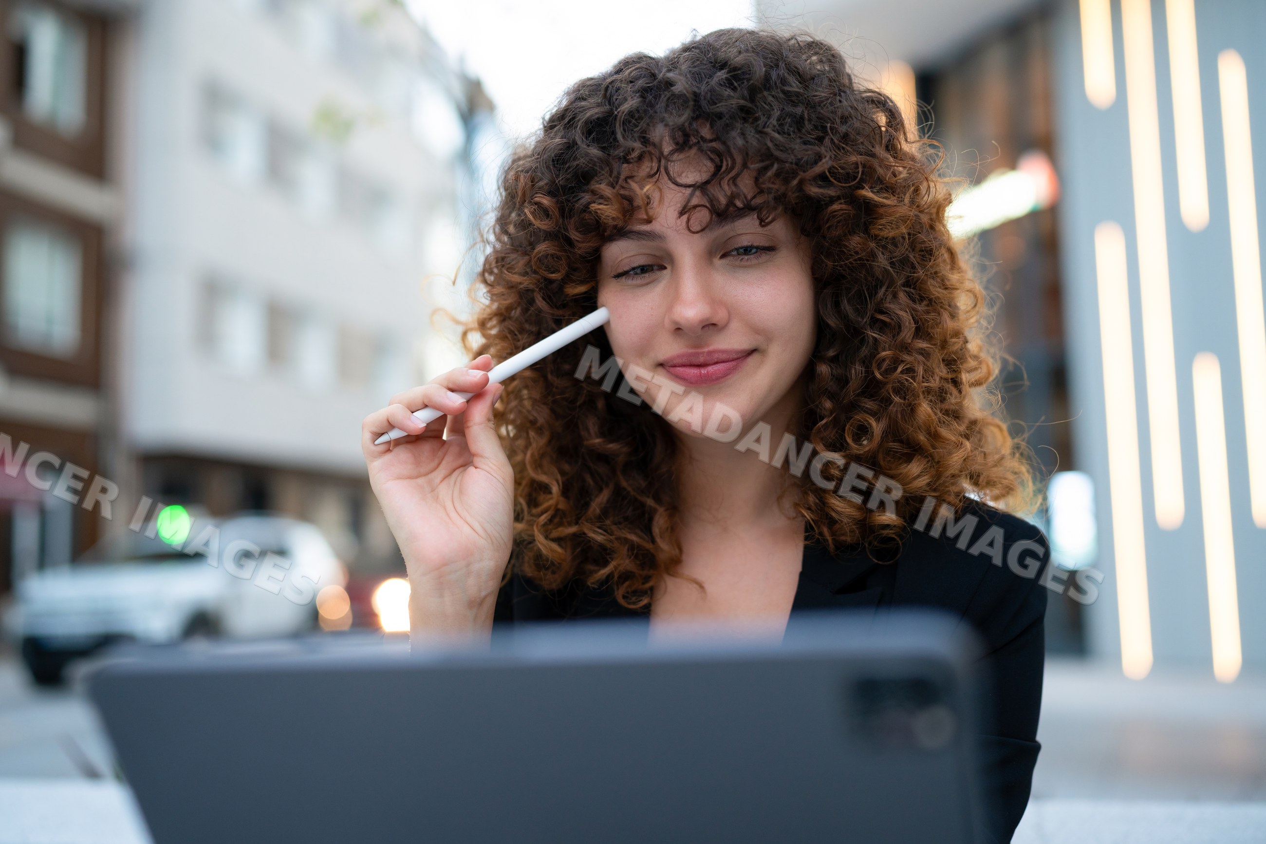 White woman with curly hair using digital tablet and stylus outdoors