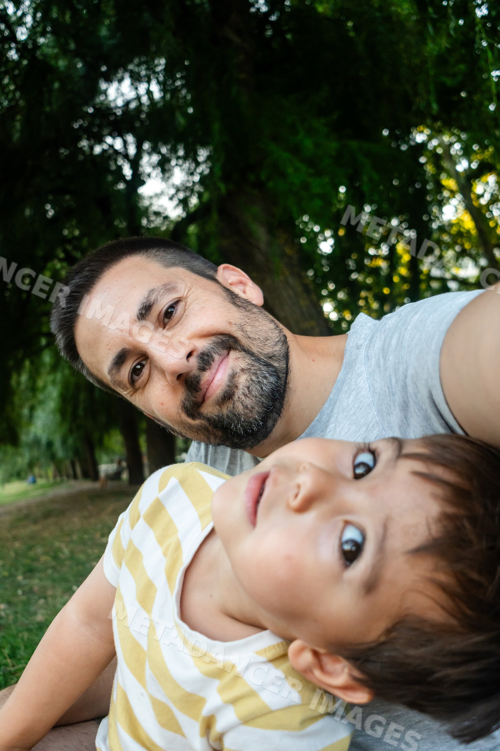 A father enjoys taking a selfie with his young son outdoors in a park