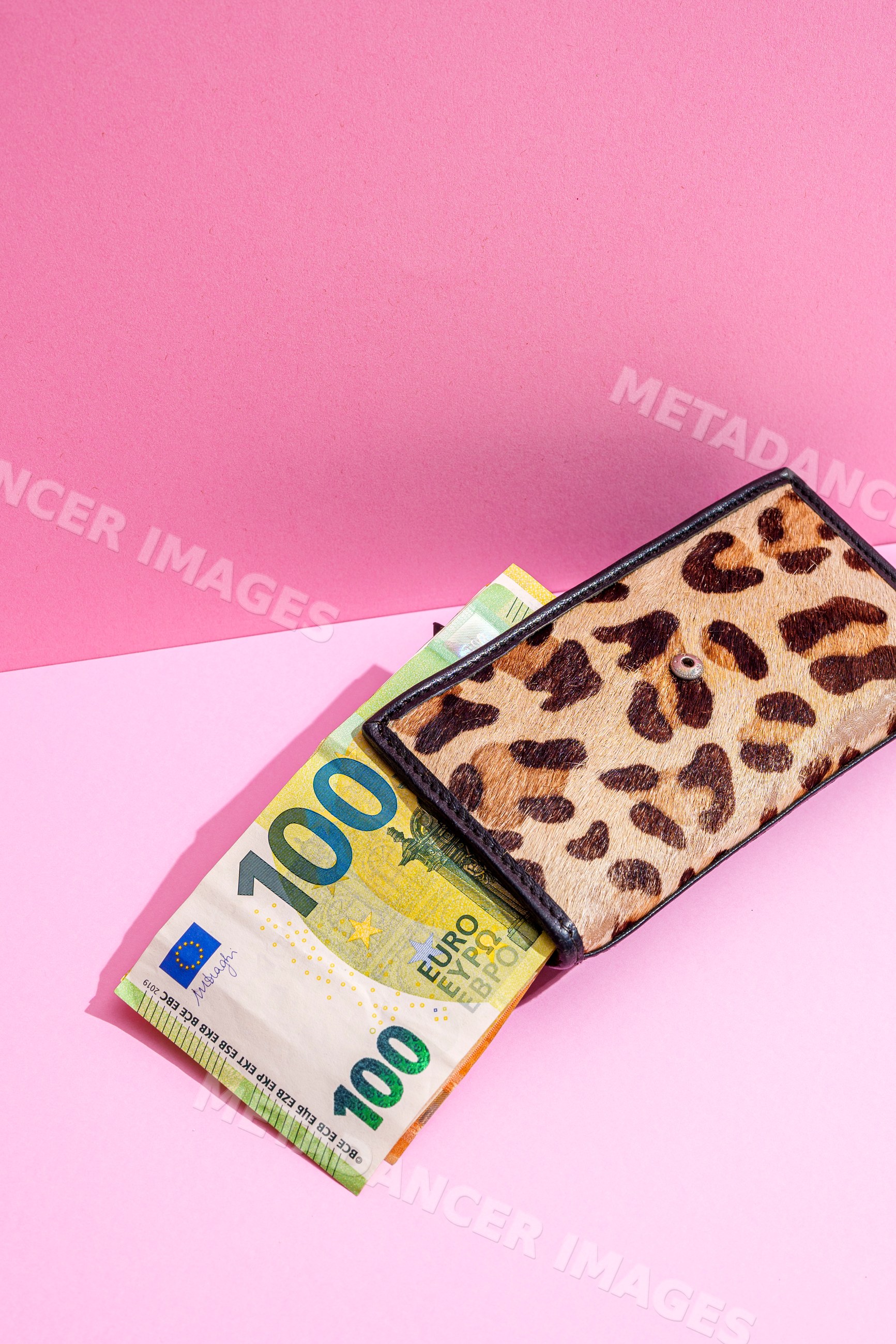 Leopard print wallet holding 100 euro banknote on pink studio