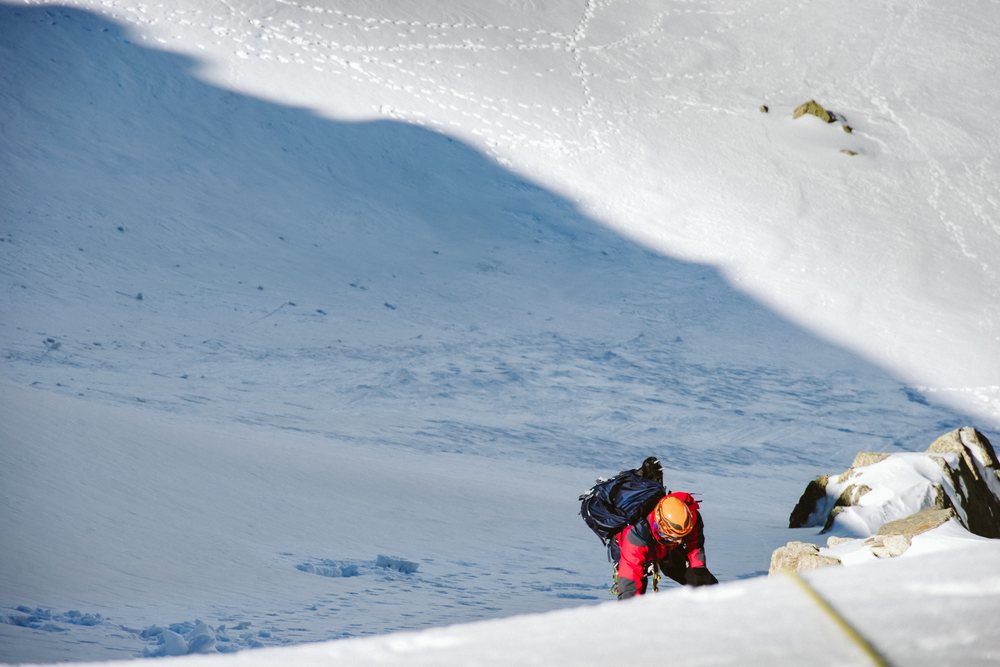 Mountaineer climbing steep snowy mountain slope with climbing gear