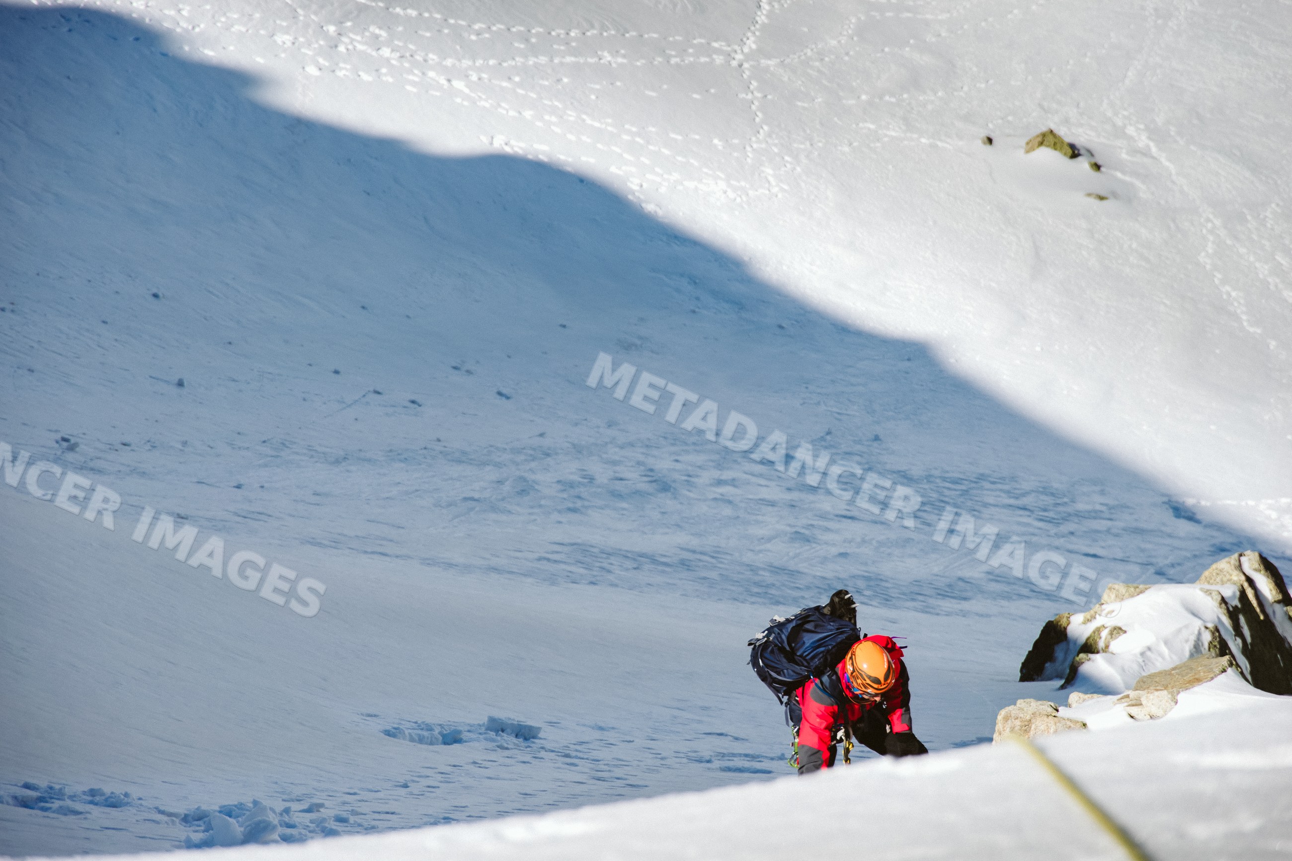 Mountaineer climbing steep snowy mountain slope with climbing gear
