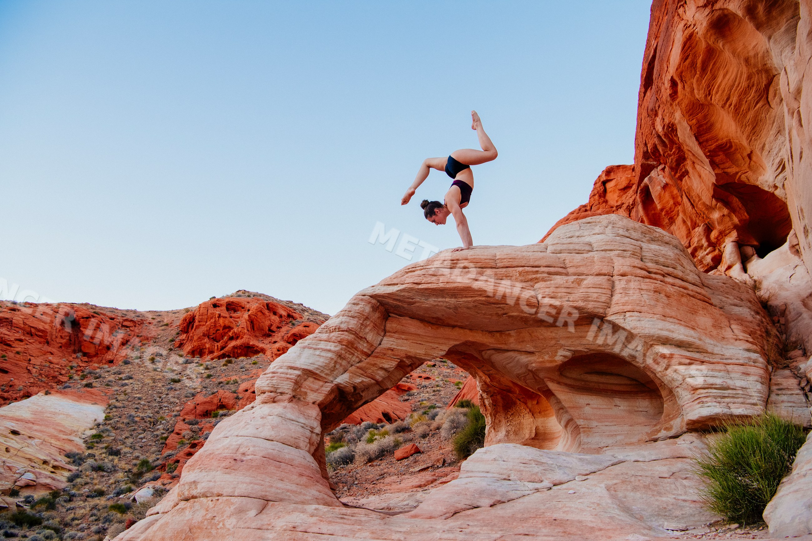 White woman doing handstand yoga pose on rock arch in desert USA